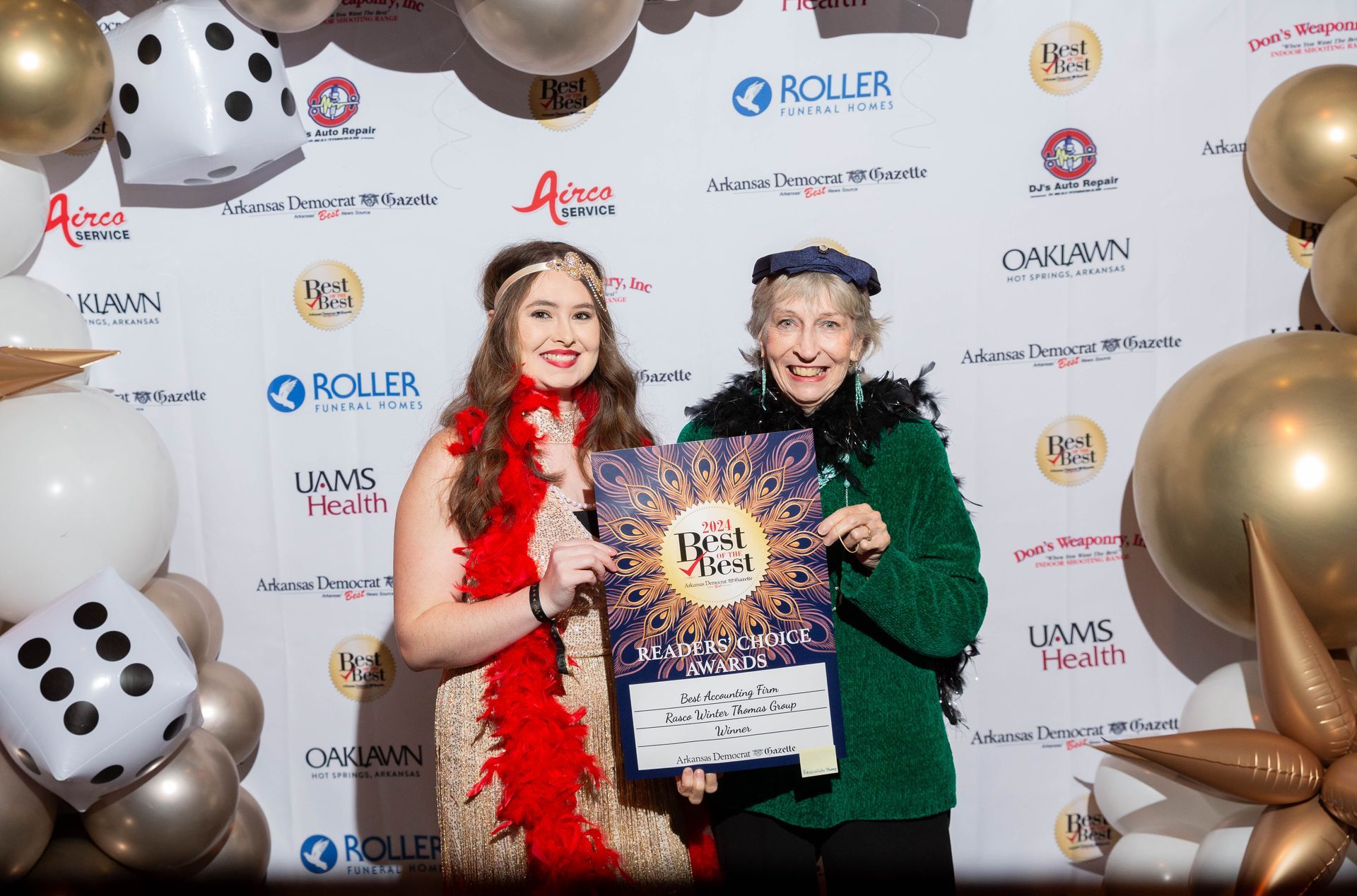 Two women are posing for a picture in front of a wall of balloons.