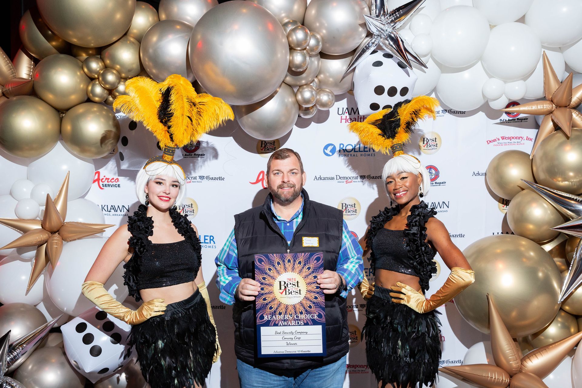 A man and two women are standing in front of a wall of balloons.