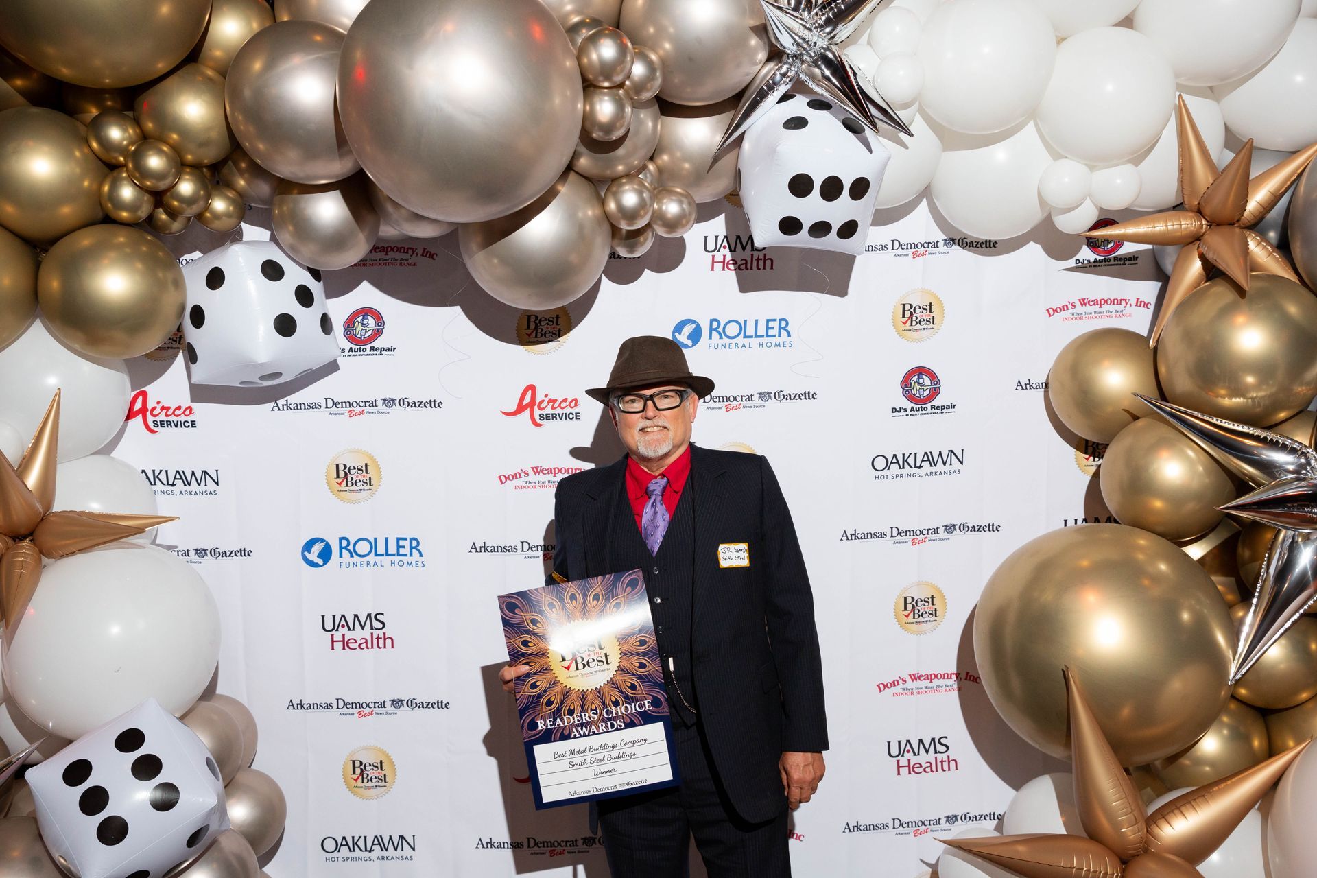 A man in a suit and hat is standing in front of a wall of balloons.