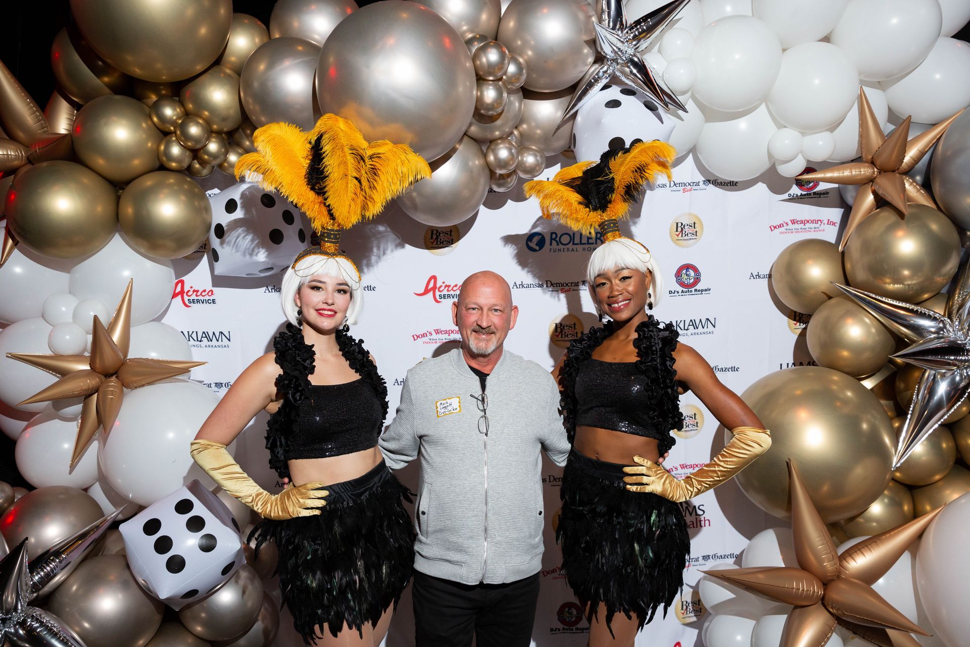 A man and two women are posing for a picture in front of a wall of balloons.