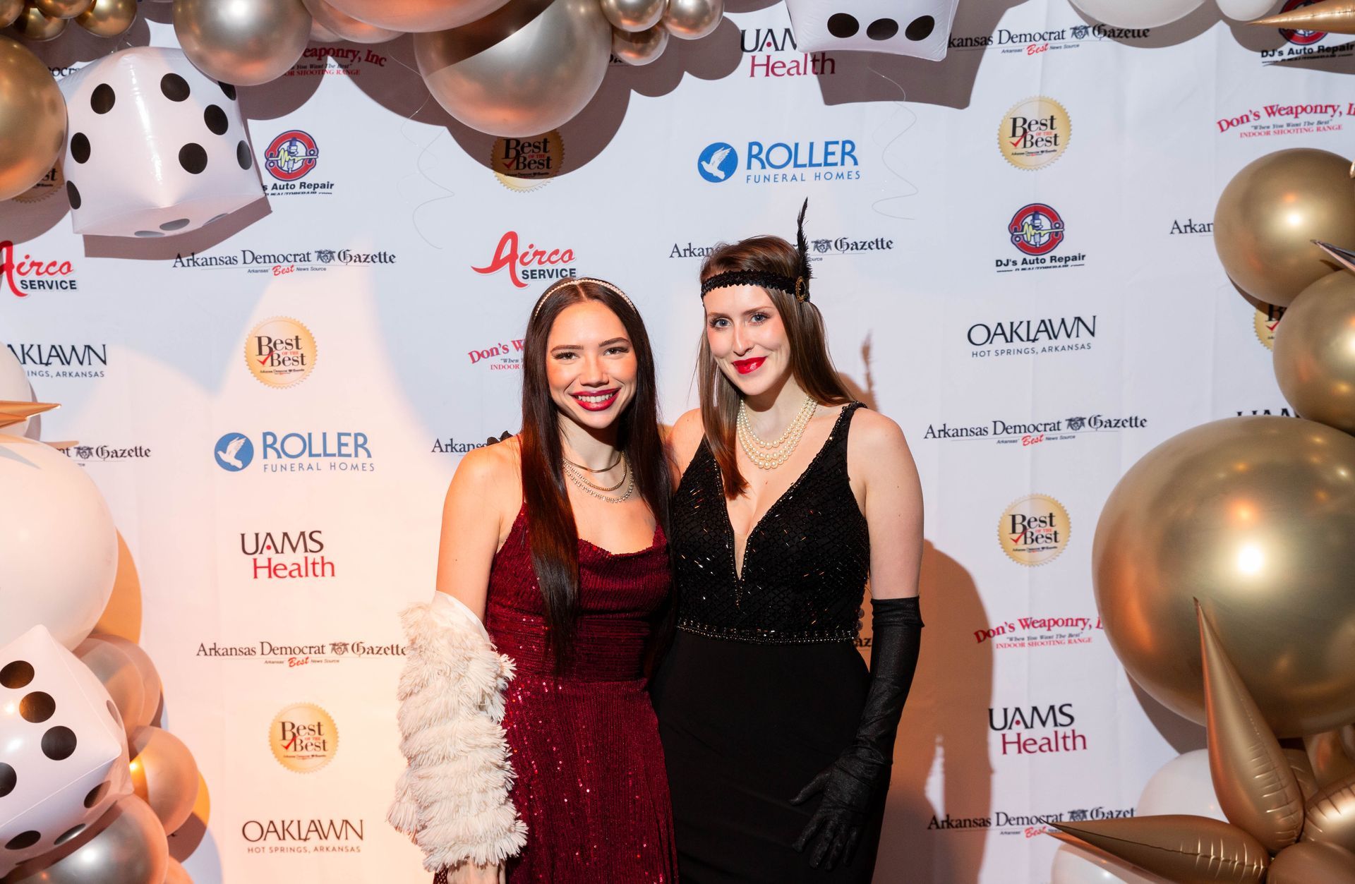 Two women are posing for a picture in front of a wall of balloons.
