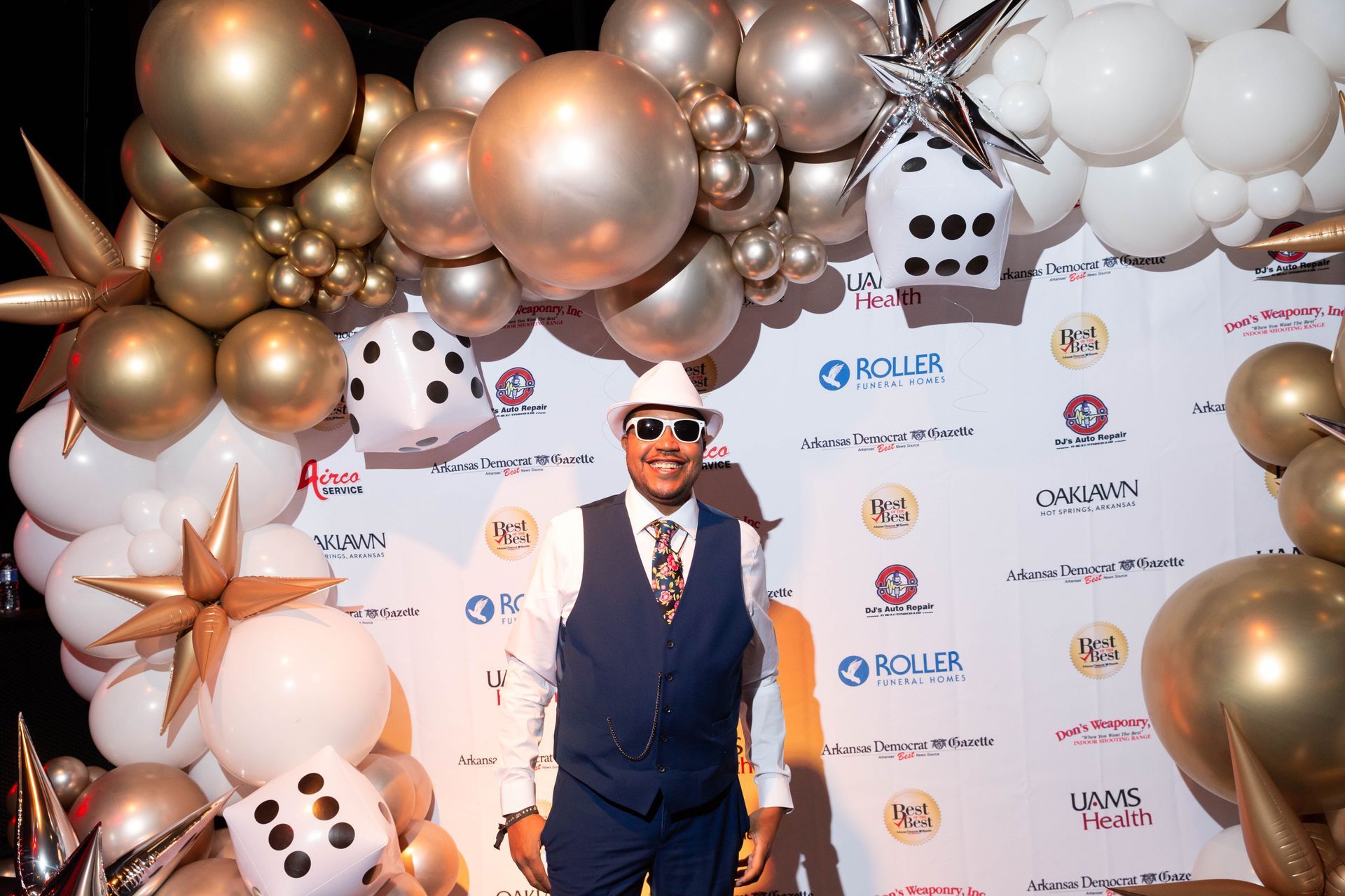 A man in a suit and hat is standing in front of a wall of balloons.