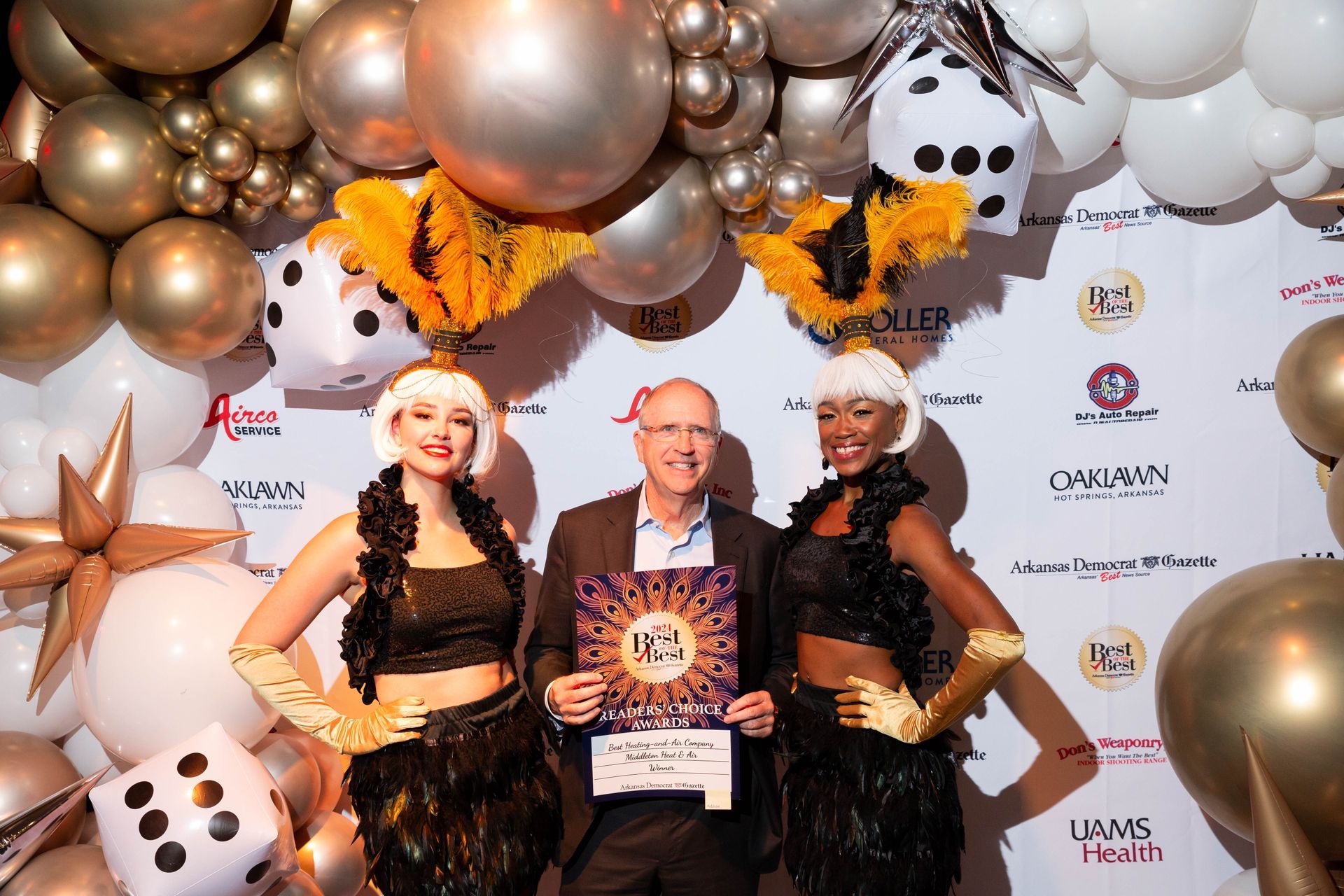 A man and two women are standing next to each other in front of a wall of balloons.