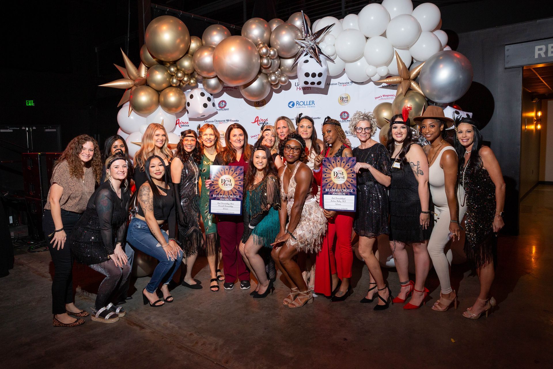 A group of women are posing for a picture in front of a wall of balloons.