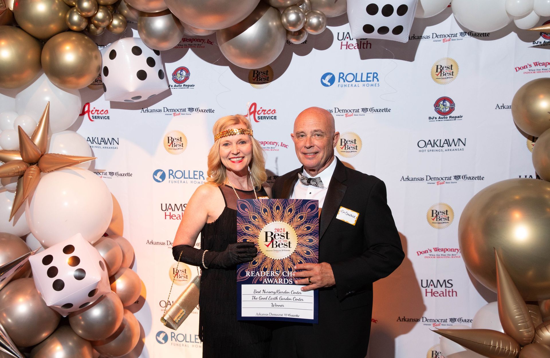 A man and a woman are posing for a picture in front of a wall of balloons.