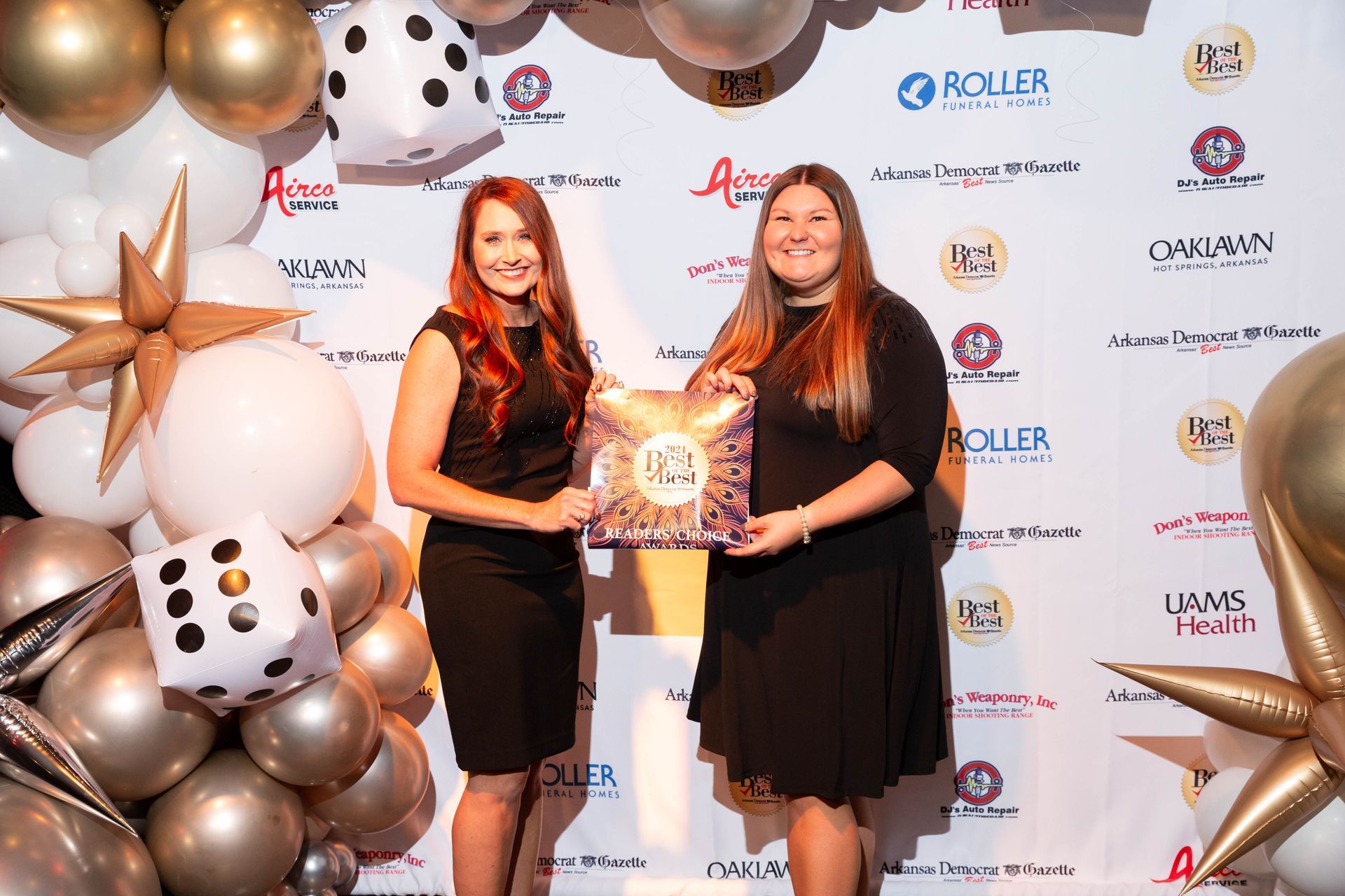 Two women are standing next to each other in front of a wall of balloons.