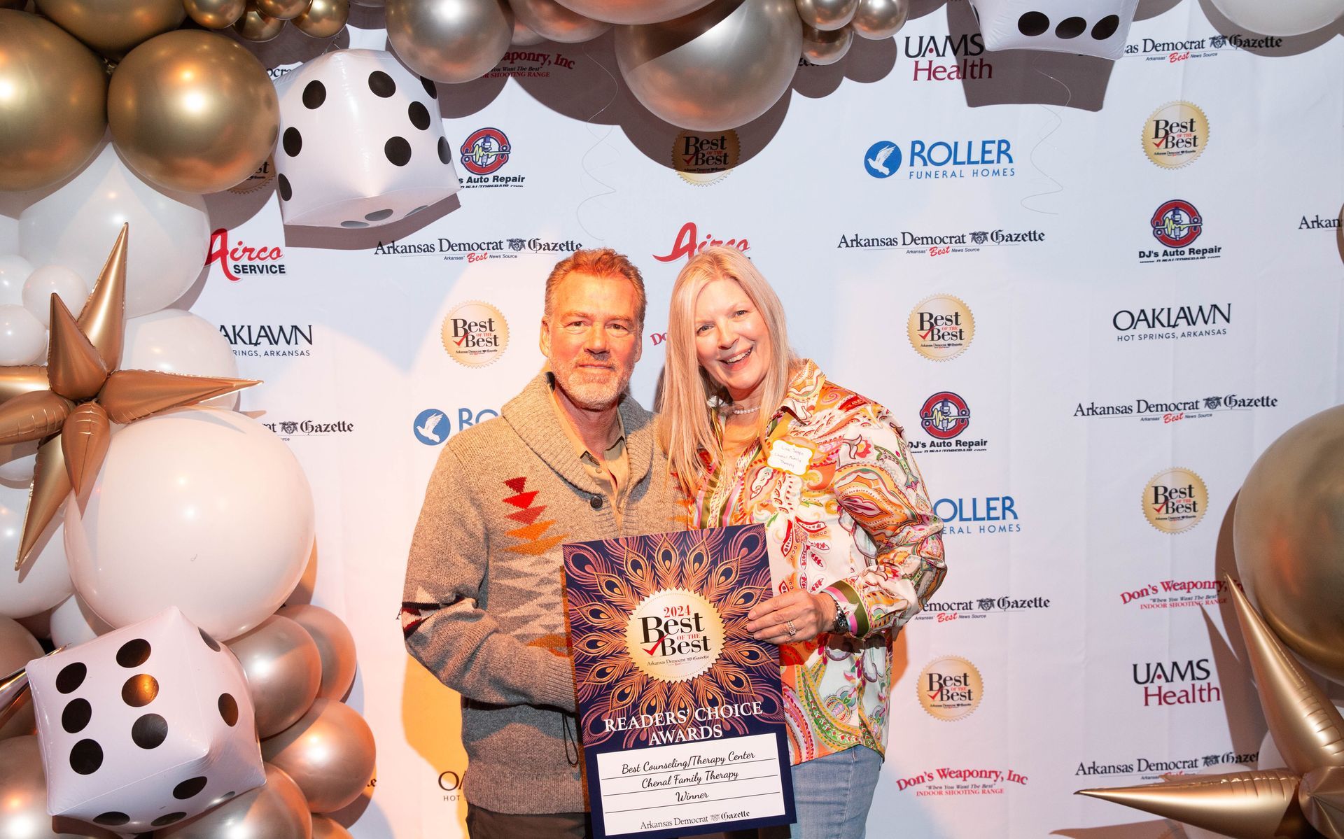 A man and a woman are standing next to each other in front of a wall of balloons.