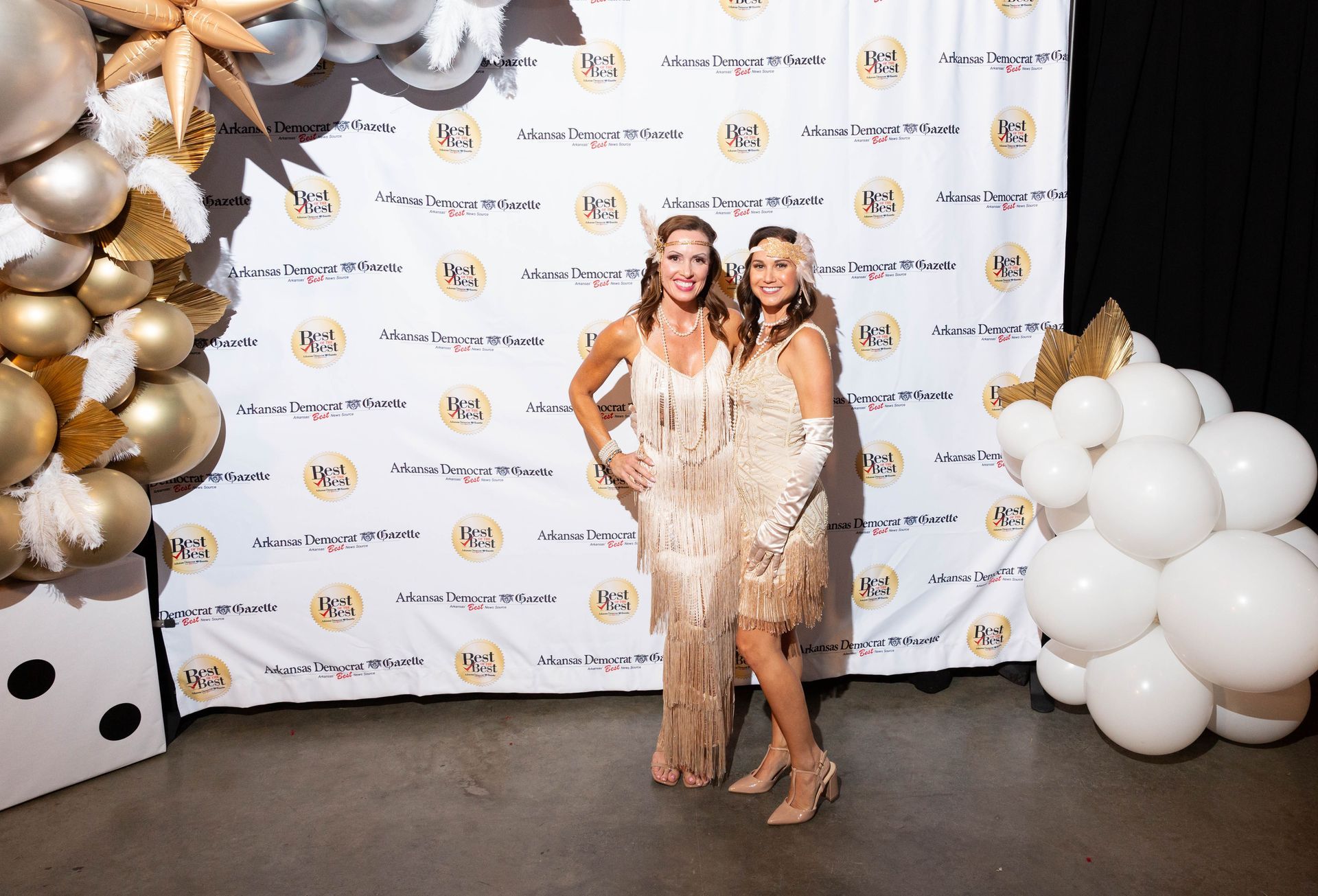 Two women are posing for a picture in front of a wall with balloons.