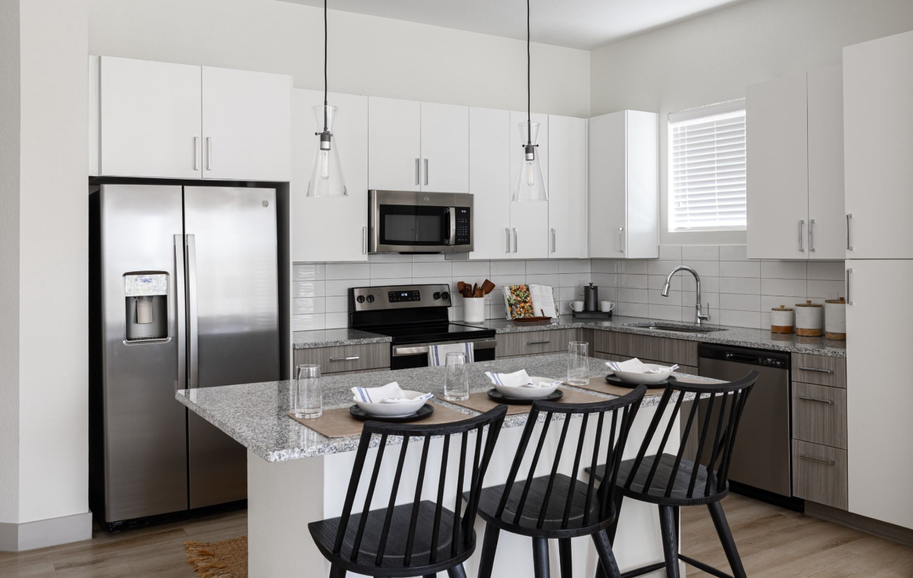 Modern kitchen with stainless steel appliances, white cabinets, and a granite island with bar stools.