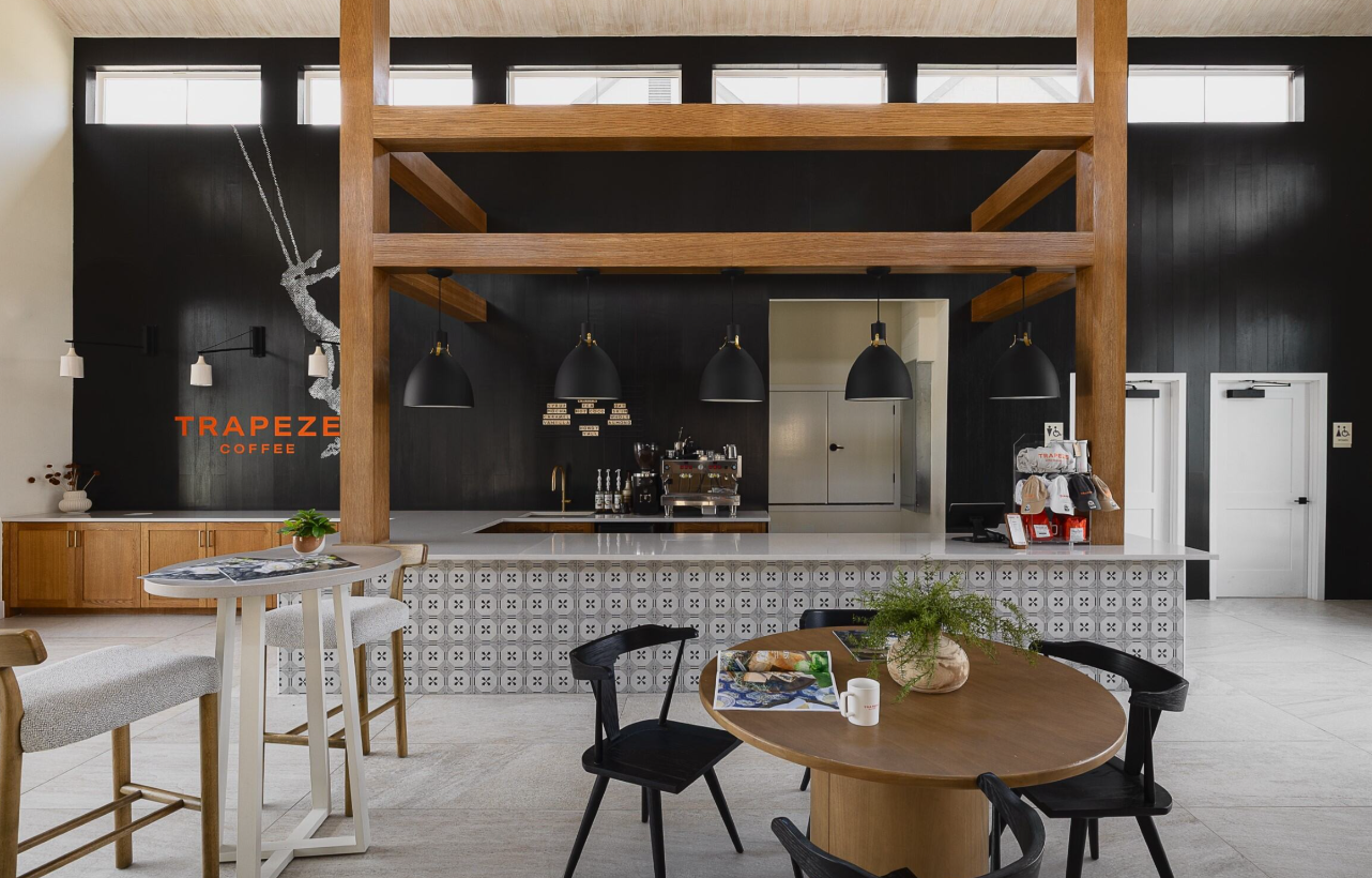 Modern café interior with wooden bar, black chairs, and hanging lights against dark walls.