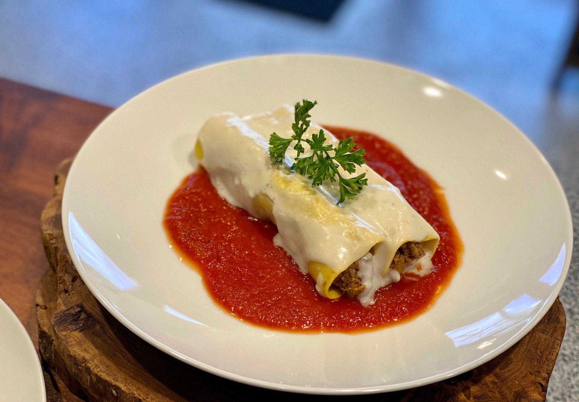 A white plate topped with a cannelloni with tomato sauce and parsley.