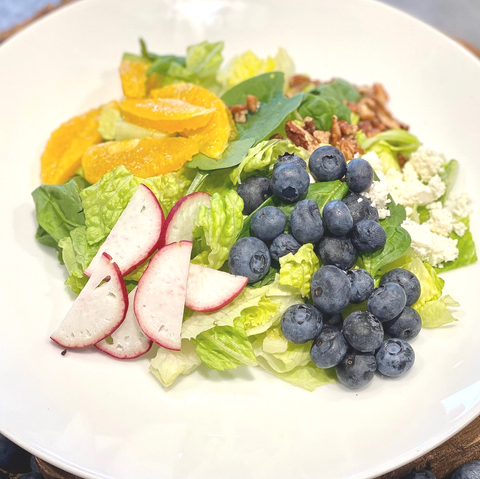 A salad with blueberries , oranges , lettuce , and cheese on a white plate.