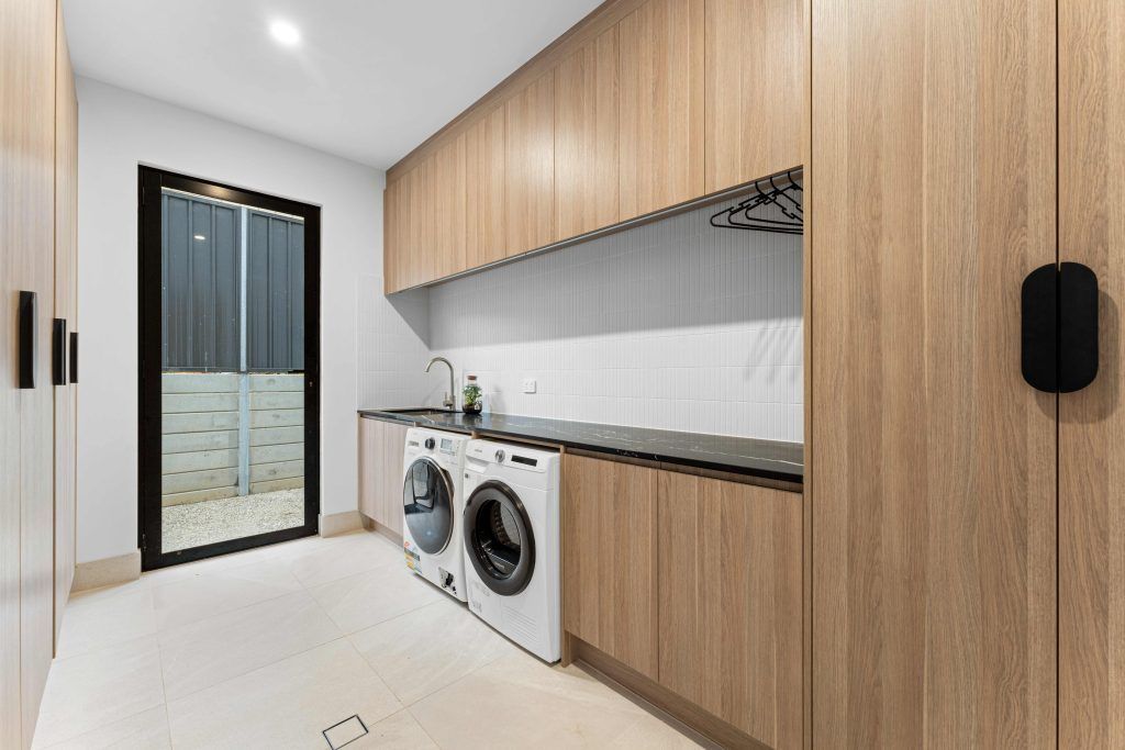 Laundry room with wood cabinets, white appliances, and a black-framed door. — Caprice Cabinets in Noosa, QLD