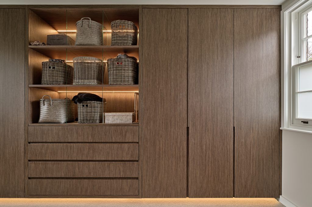 Built-in wooden closet with open shelves holding baskets and drawers. Doors on right, window on right. — Caprice Cabinets in Noosa, QLD
