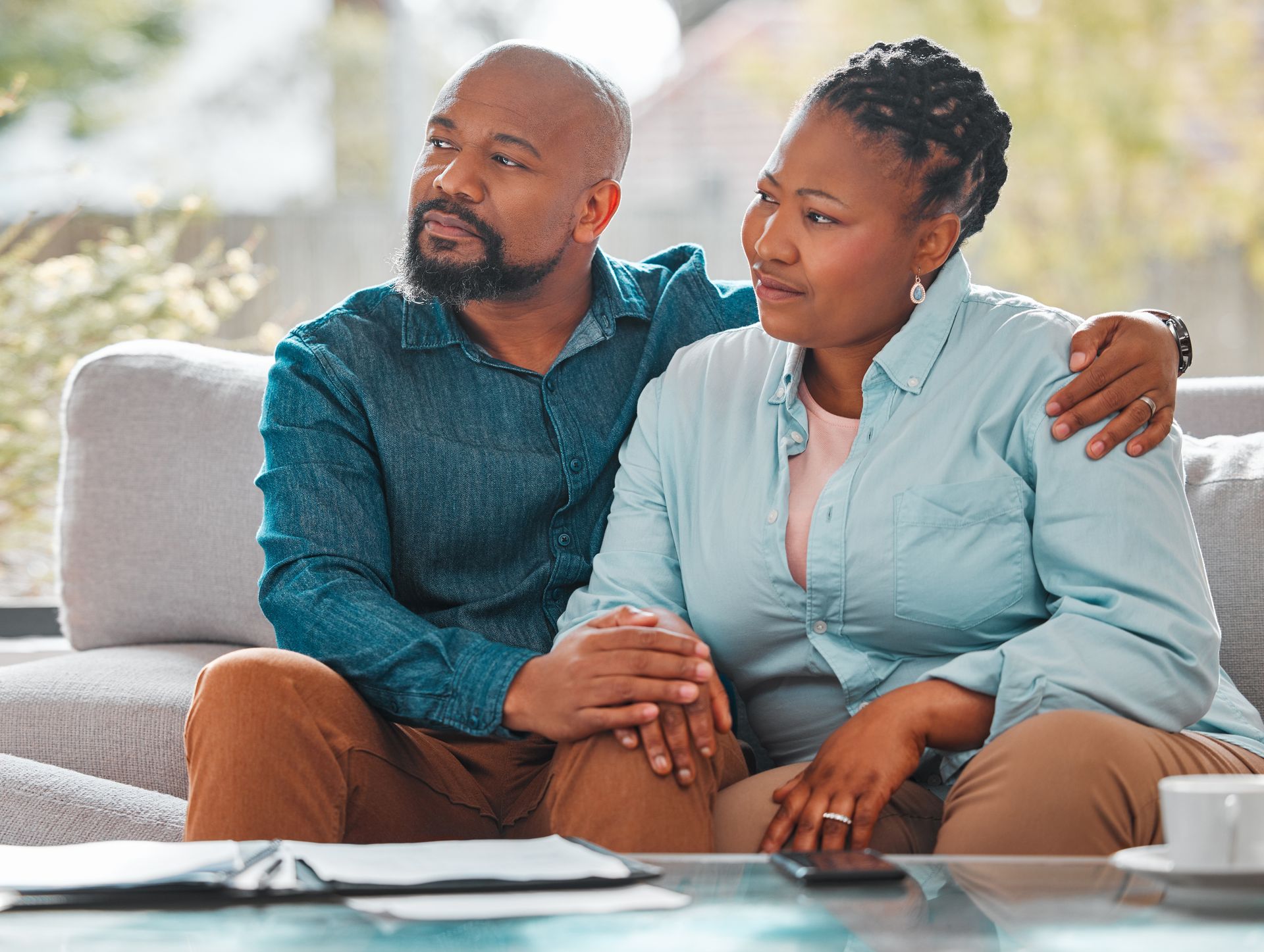 Couple sitting on a couch, man with arm around woman, looking out the window.