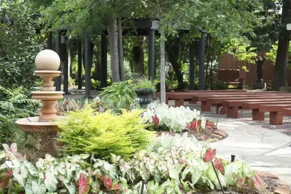 Garden courtyard with flower beds, stone benches, and leafy trees along a paved path