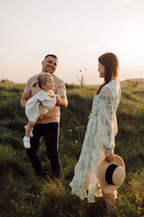 Family standing in a grassy field at sunset, with a baby and a hat in the foreground.
