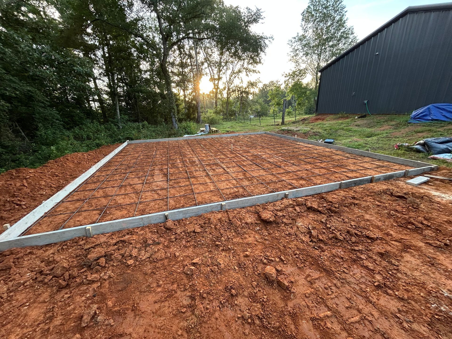 A rectangular perimeter of concrete blocks set on red dirt for a foundation, with a dark building in the background.