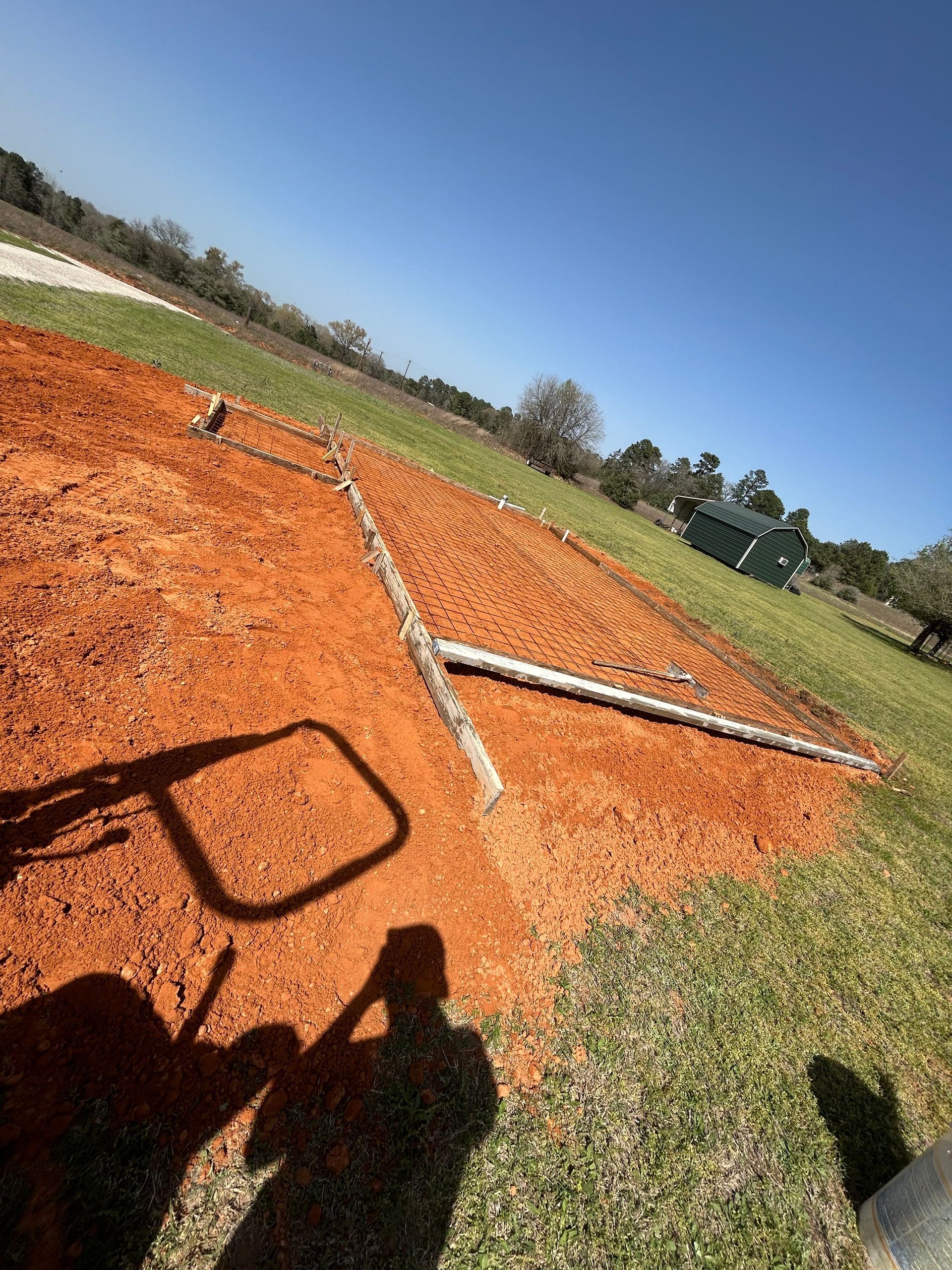 A Y-shaped log lies in a patch of freshly turned reddish-orange soil on a grassy hillside under a clear blue sky.