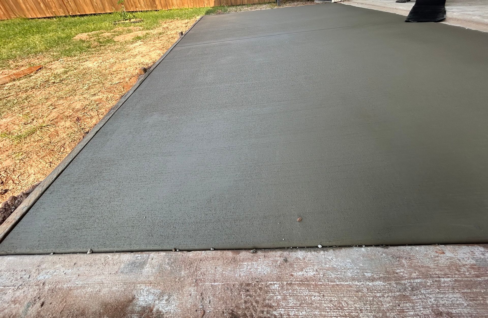 Freshly poured gray concrete slab adjacent to a grass lawn and an existing walkway.