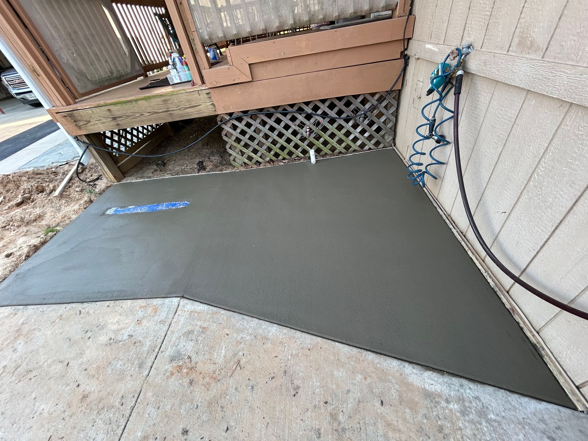 A newly poured concrete slab sits at the base of a wooden deck, meeting an existing concrete patio.