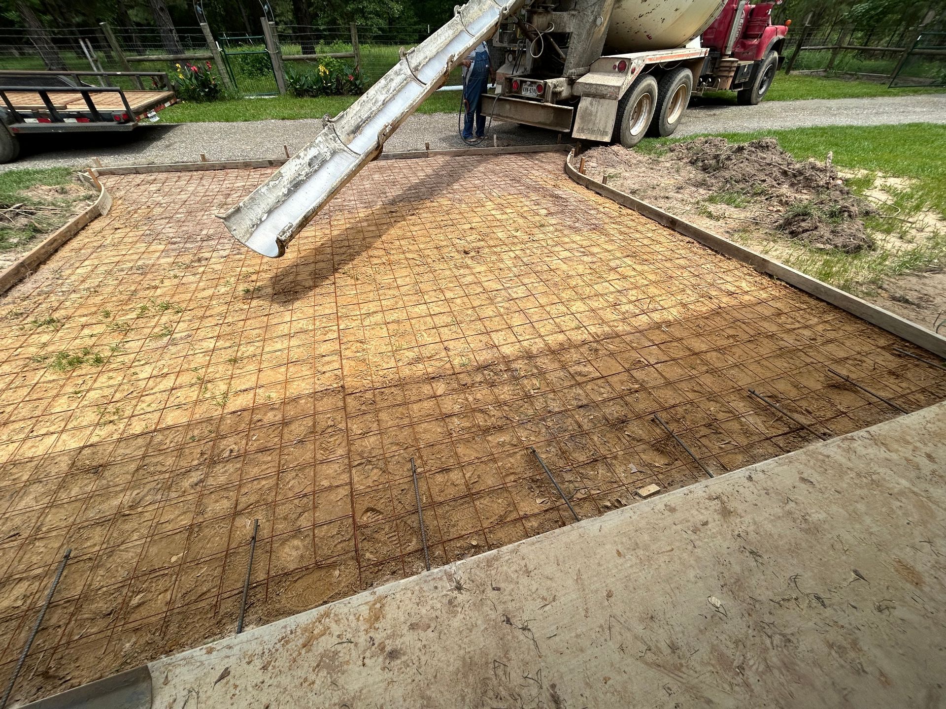 A concrete mixer truck pours wet cement onto a wire-reinforced gravel base bordered by wooden forms.