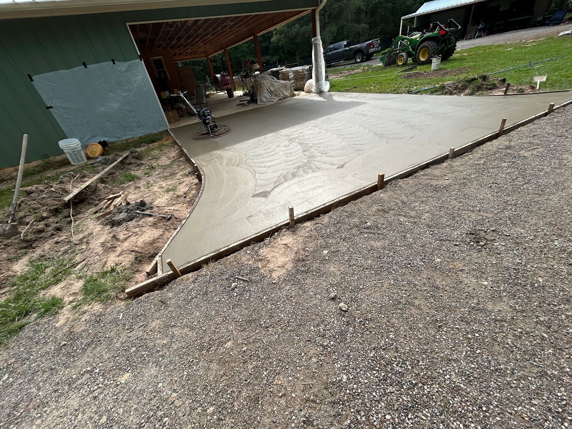A freshly poured concrete slab extends from under a covered building entrance toward a gravel driveway.