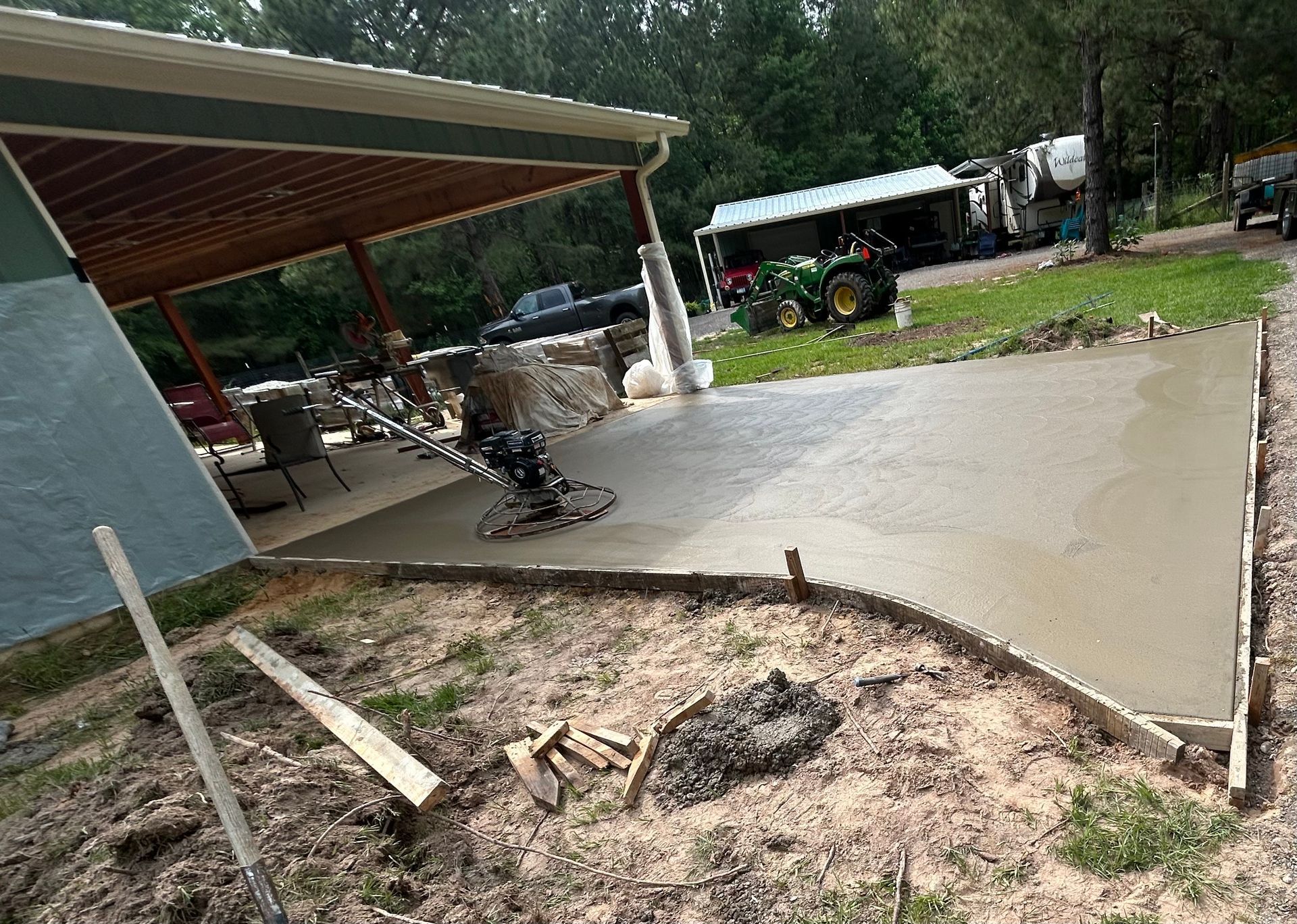 Fresh concrete patio poured under a covered porch with a power trowel and construction materials nearby.