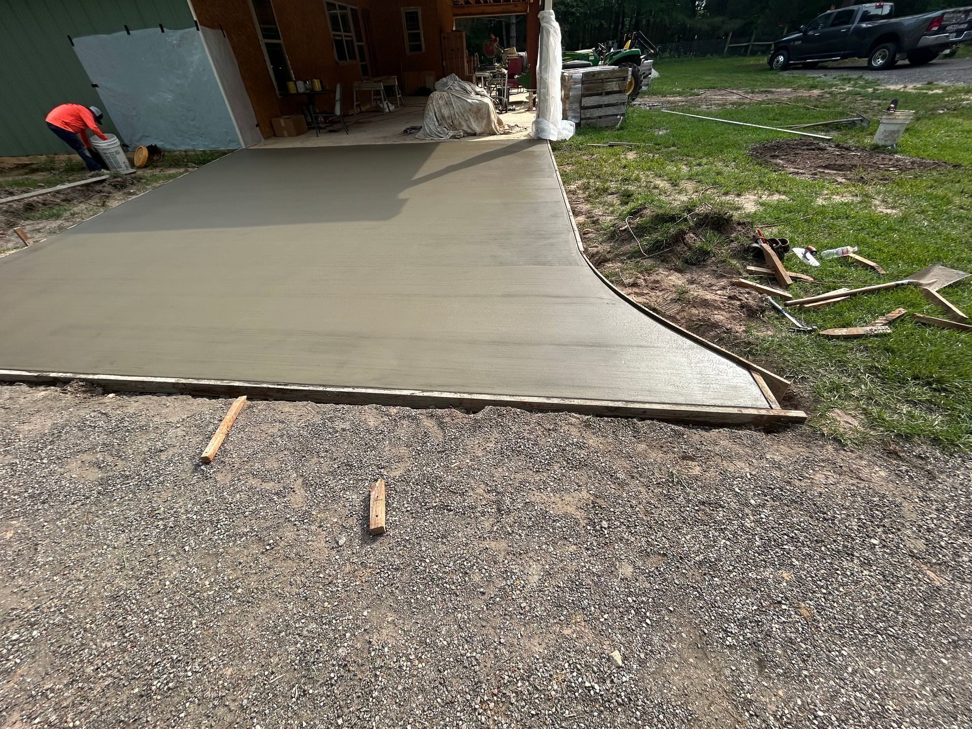 A freshly poured concrete driveway or patio section under construction in a yard, with a person working nearby.
