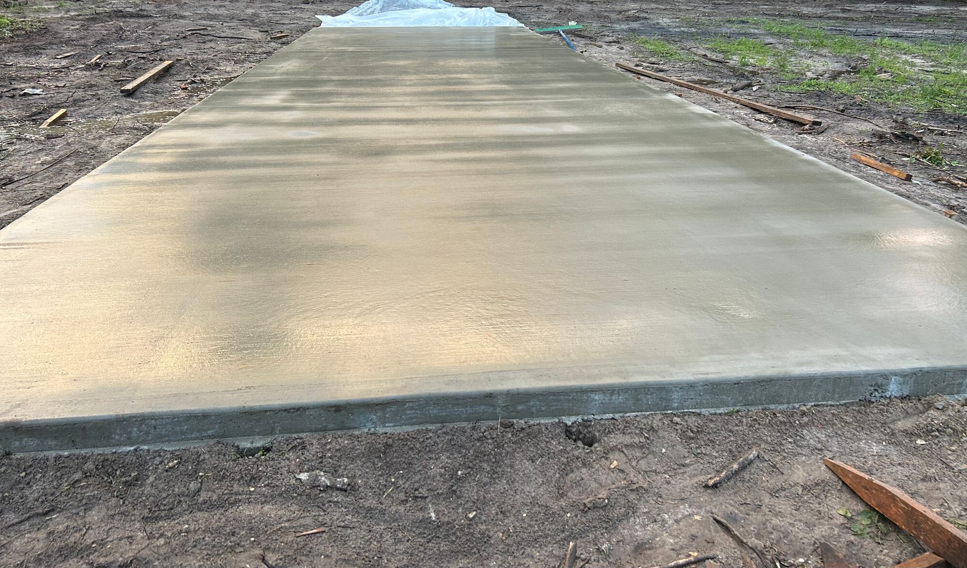 A newly poured, smooth gray concrete sidewalk extending into the distance, set in an unfinished, dirt-covered outdoor area.
