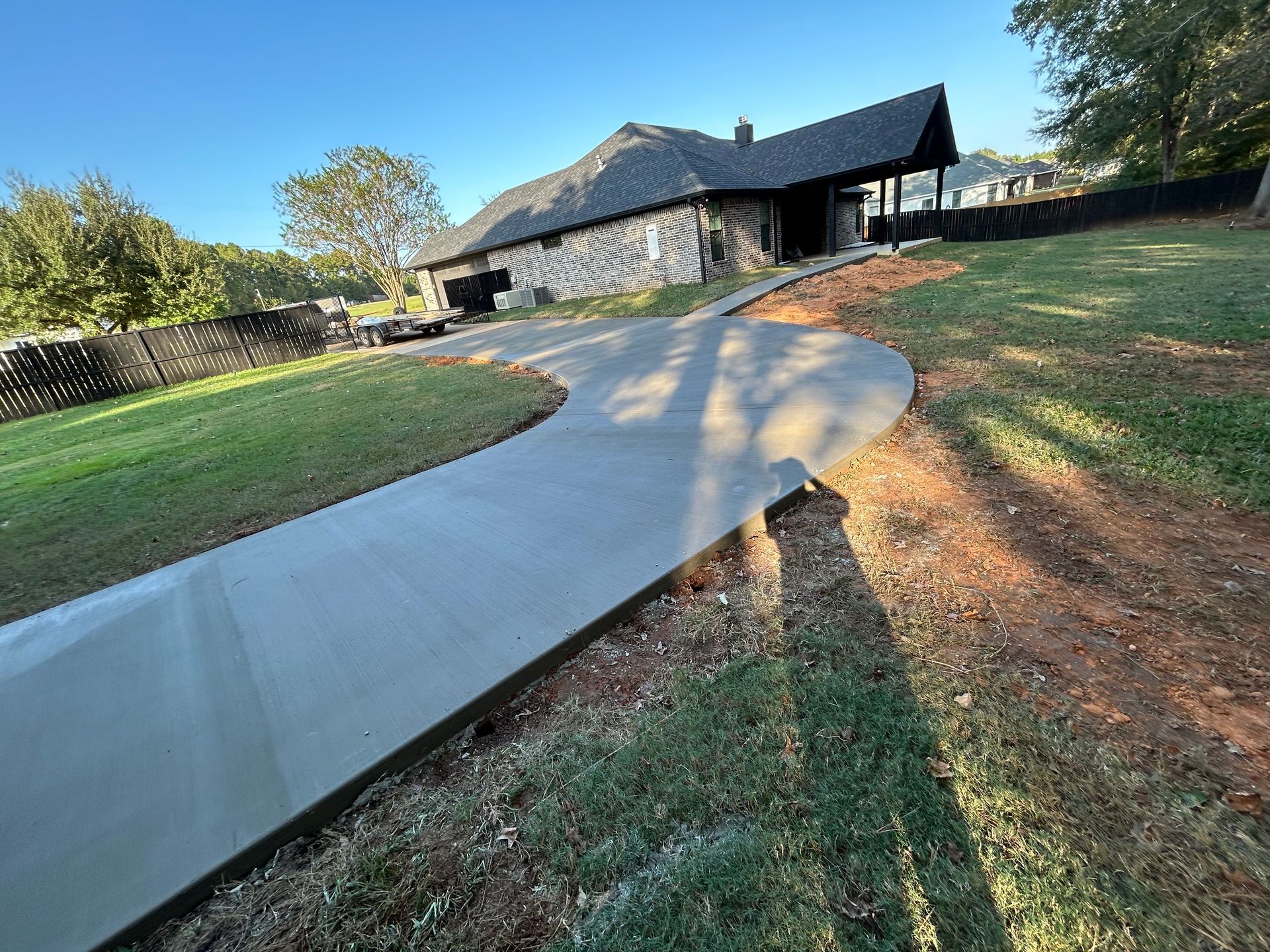 A newly poured curved concrete driveway leads to a house with a covered entryway under a clear blue sky.
