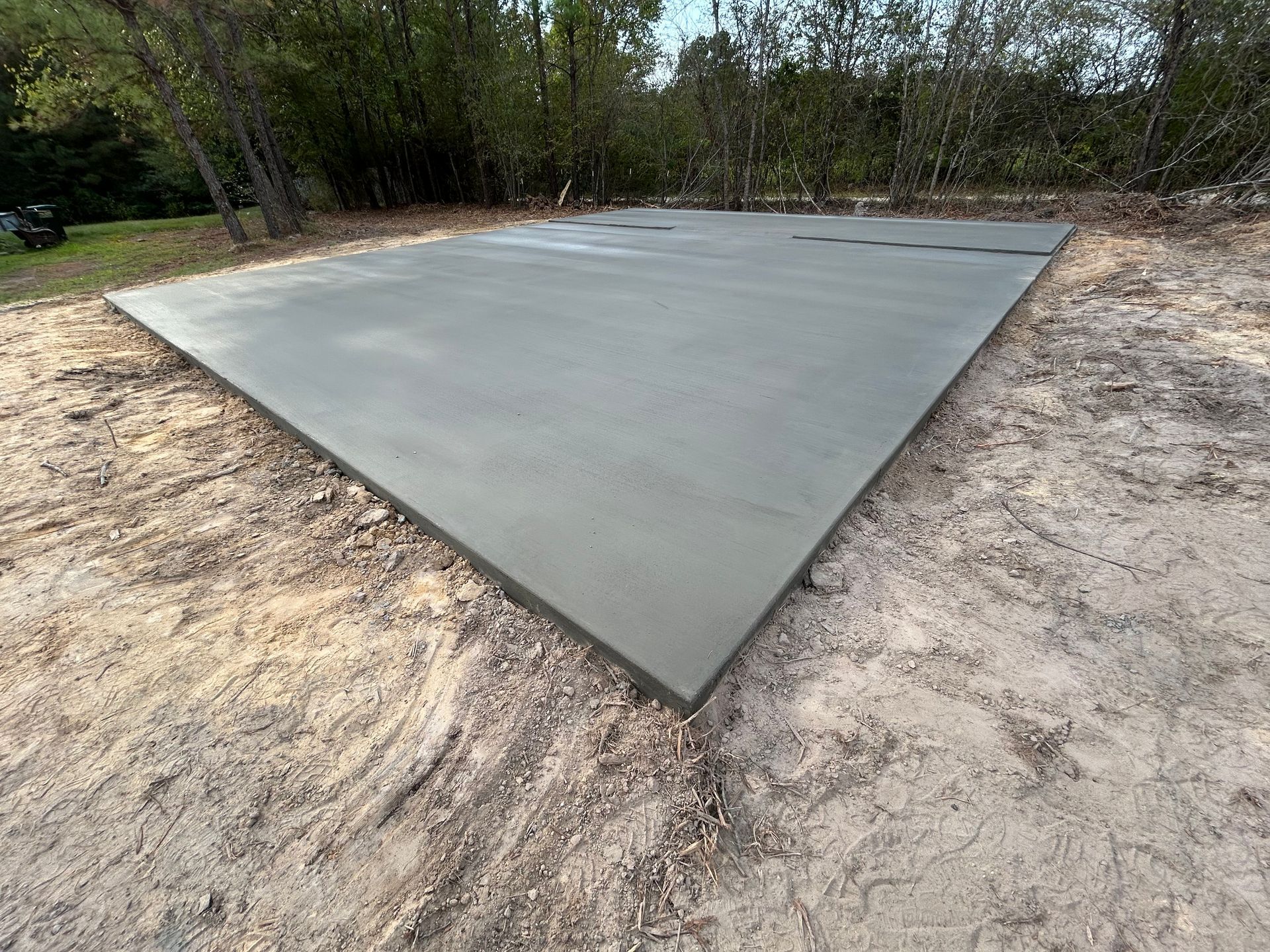 A smooth, rectangular concrete slab poured on a sandy, wooded lot.