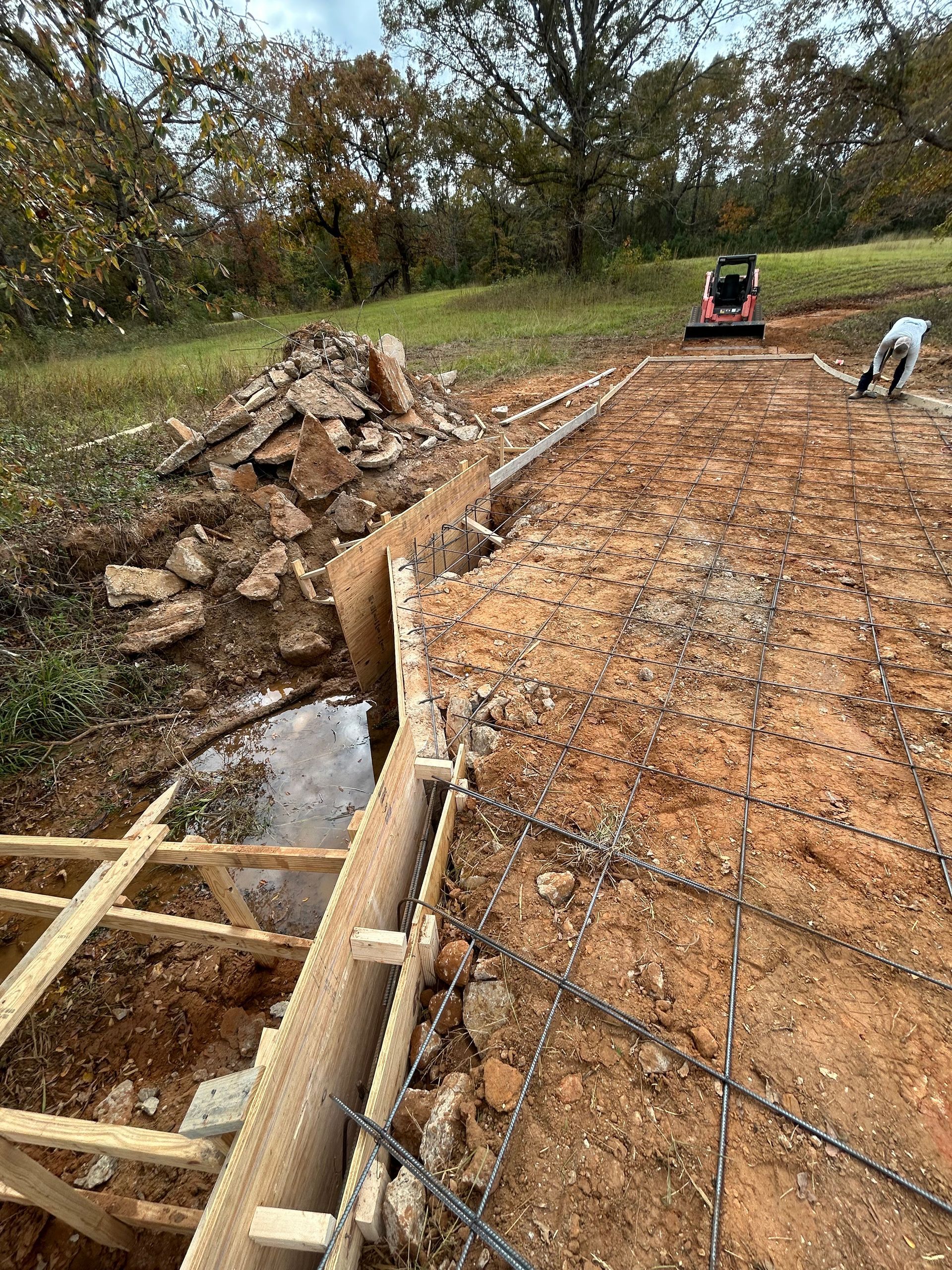 Construction site featuring a wooden form for a concrete foundation, wire mesh reinforcement, and a small utility vehicle.