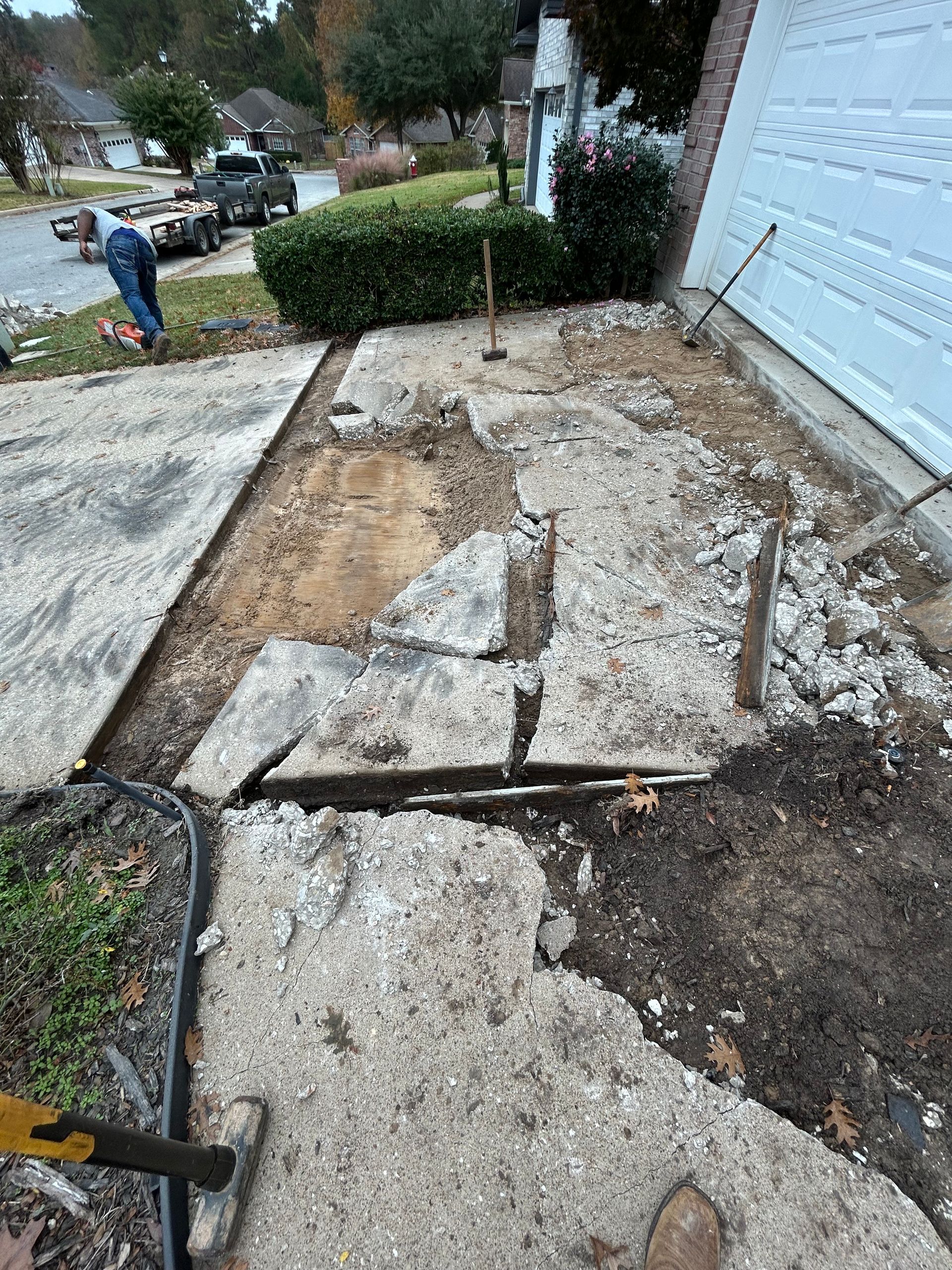 A person in a residential driveway demolishing a section of cracked concrete near a garage door.