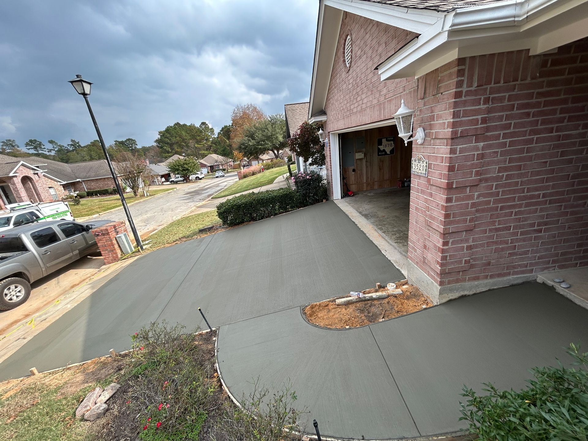 Newly poured concrete driveway and walkway leading to a brick garage in a residential neighborhood under a cloudy sky.