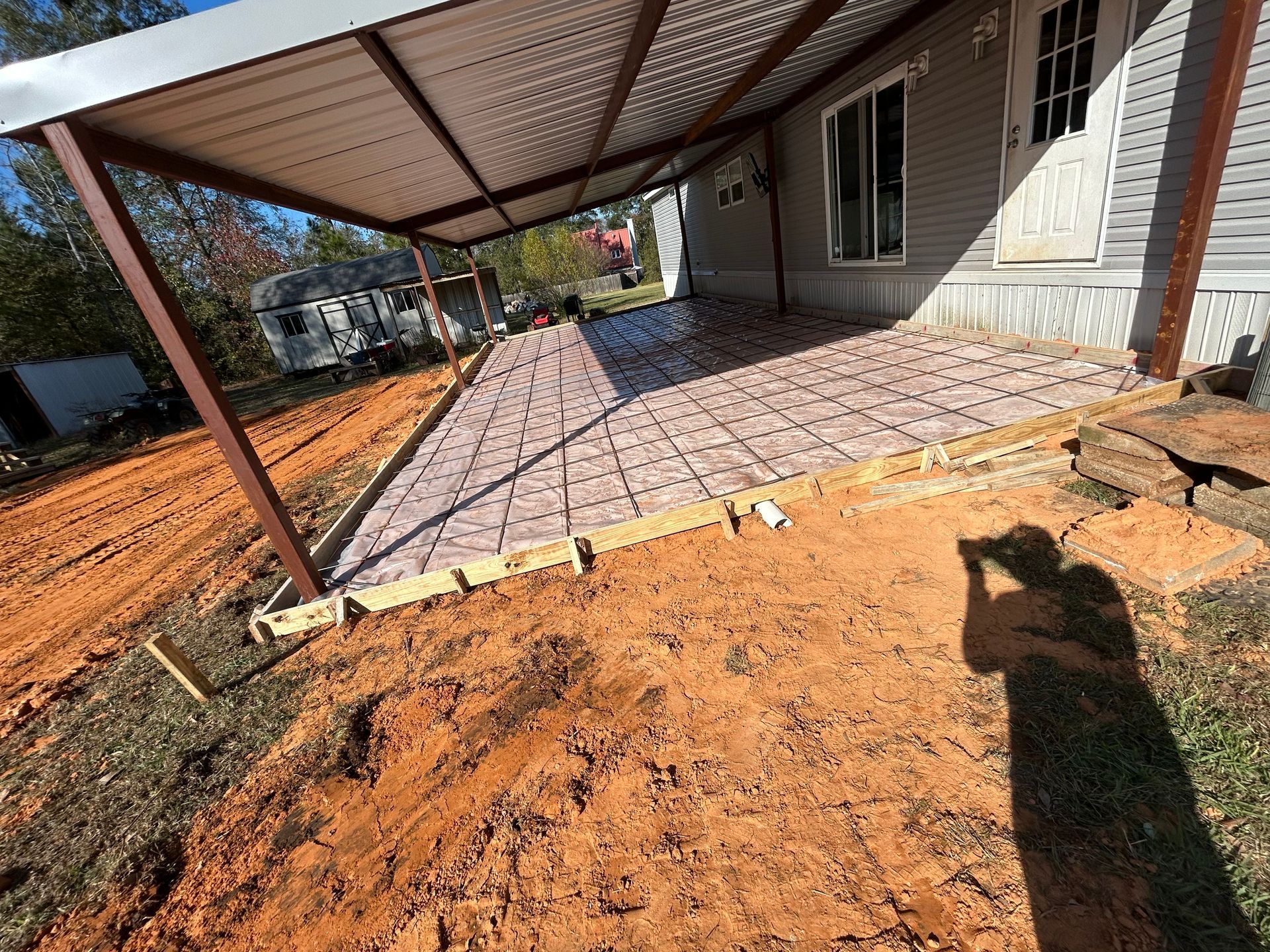 A concrete patio project under a metal carport roof with wire mesh reinforcement laid over insulation on the ground.