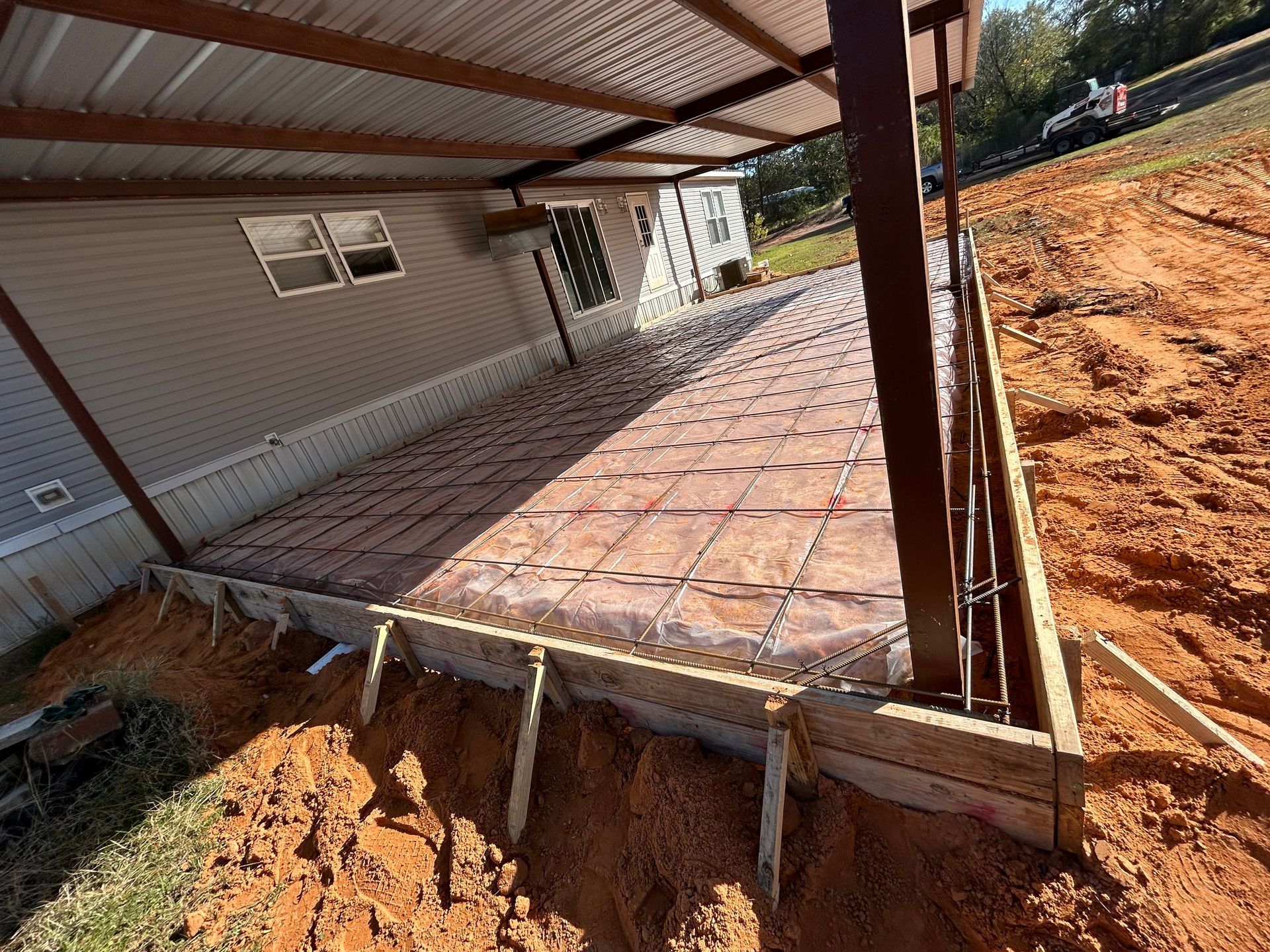 A construction site showing a prepared wooden form for a concrete patio with metal wire mesh laid on leveled dirt.
