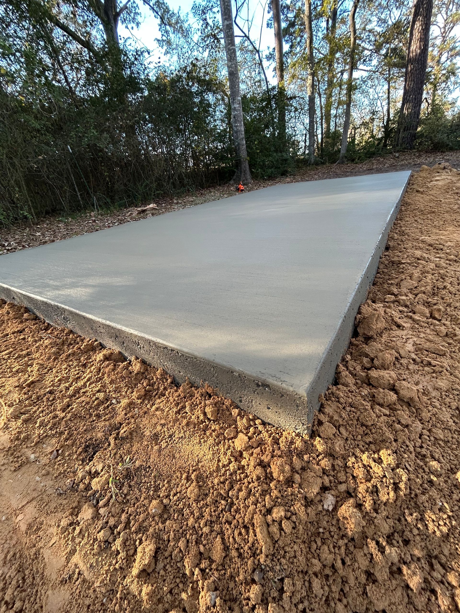 A rectangular concrete slab set in a clearing of bare soil, surrounded by trees on a sunny day.