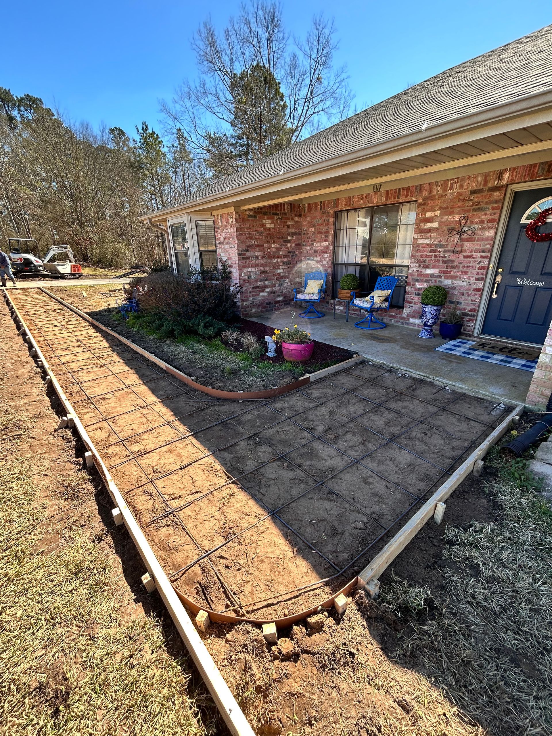 A house front yard under construction with wooden forms outlining a new sidewalk, exposed wire mesh, and soil.