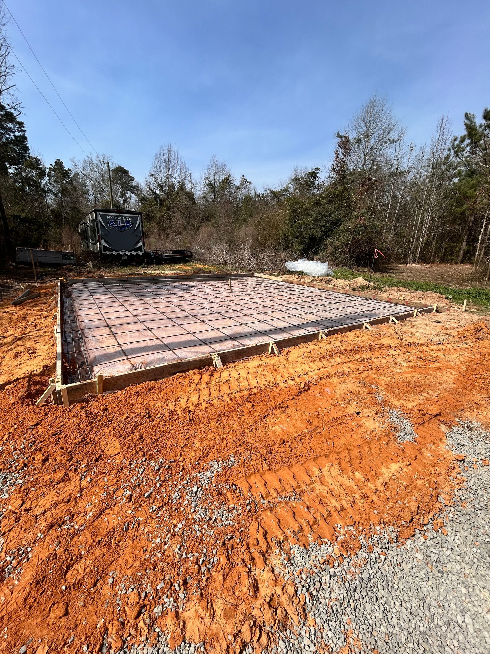 A square concrete slab under construction, framed with wooden boards and covered with a plastic vapor barrier.
