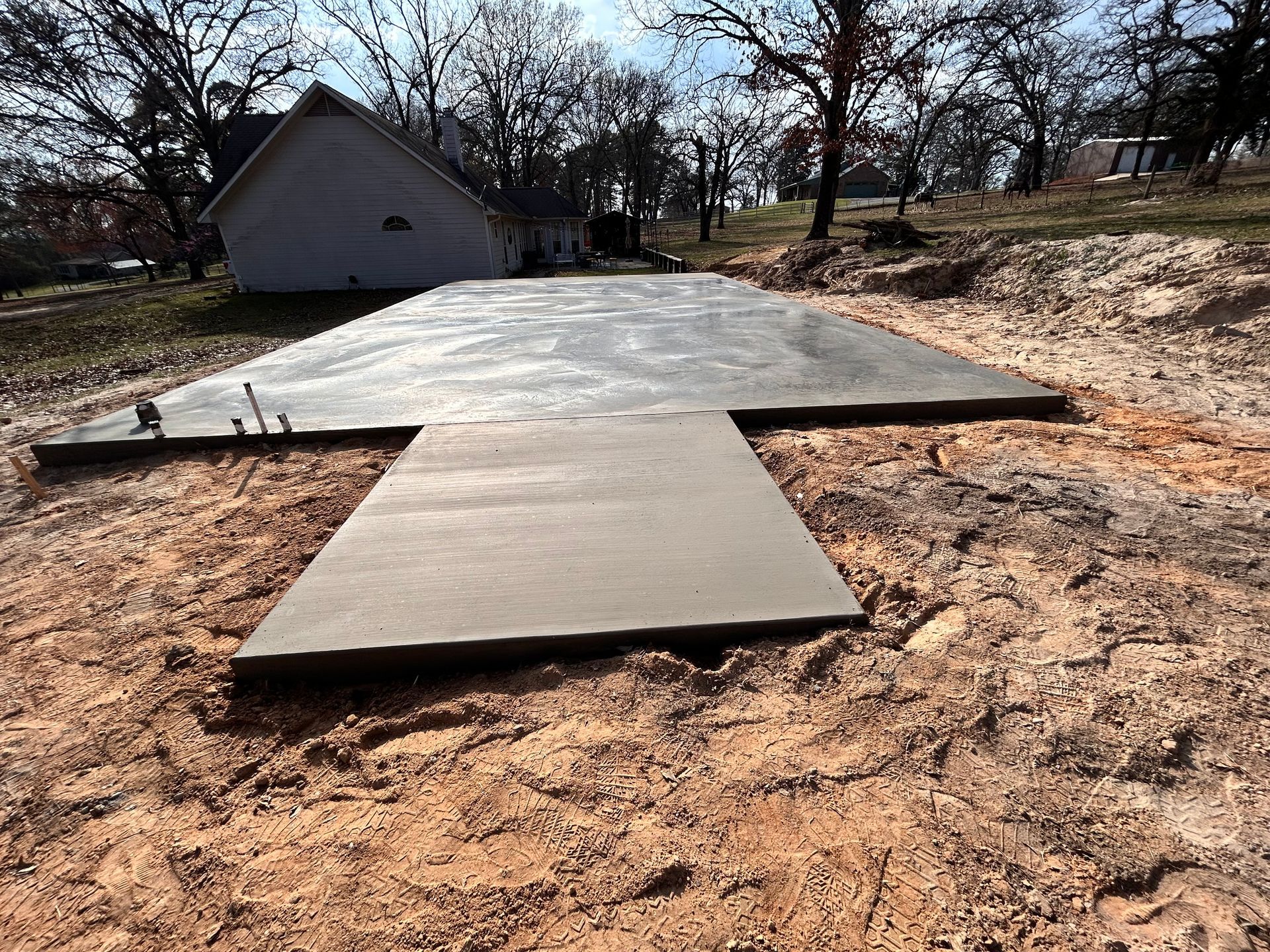 A newly poured concrete foundation and walkway slab surrounded by dirt on an outdoor construction site.