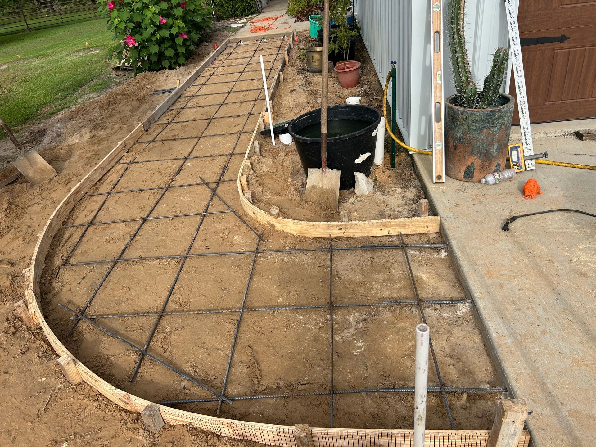 A wooden-formed walkway preparation for concrete, featuring a metal wire grid laid over sand in a residential yard.