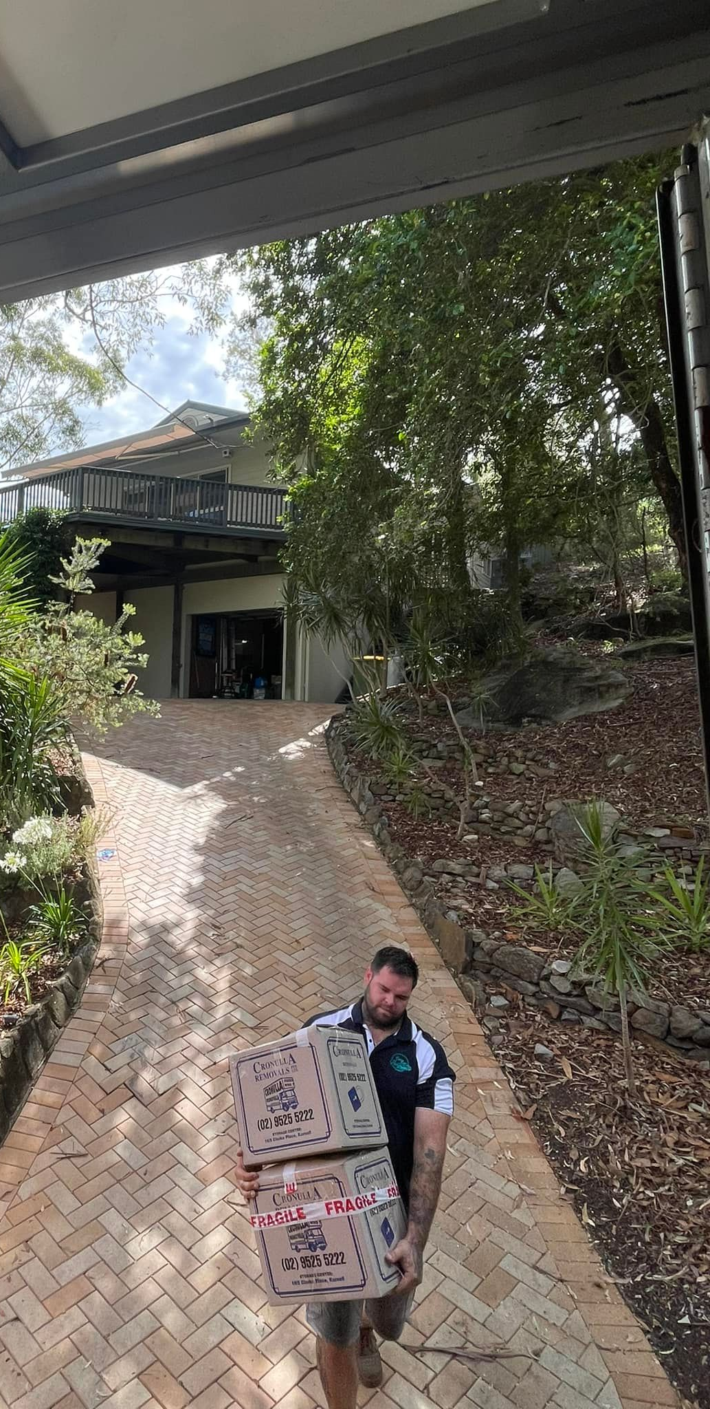 A person carrying a large bag walks up a brick path toward a house surrounded by trees. — Easy Flow Removals In Wauchope, NSW