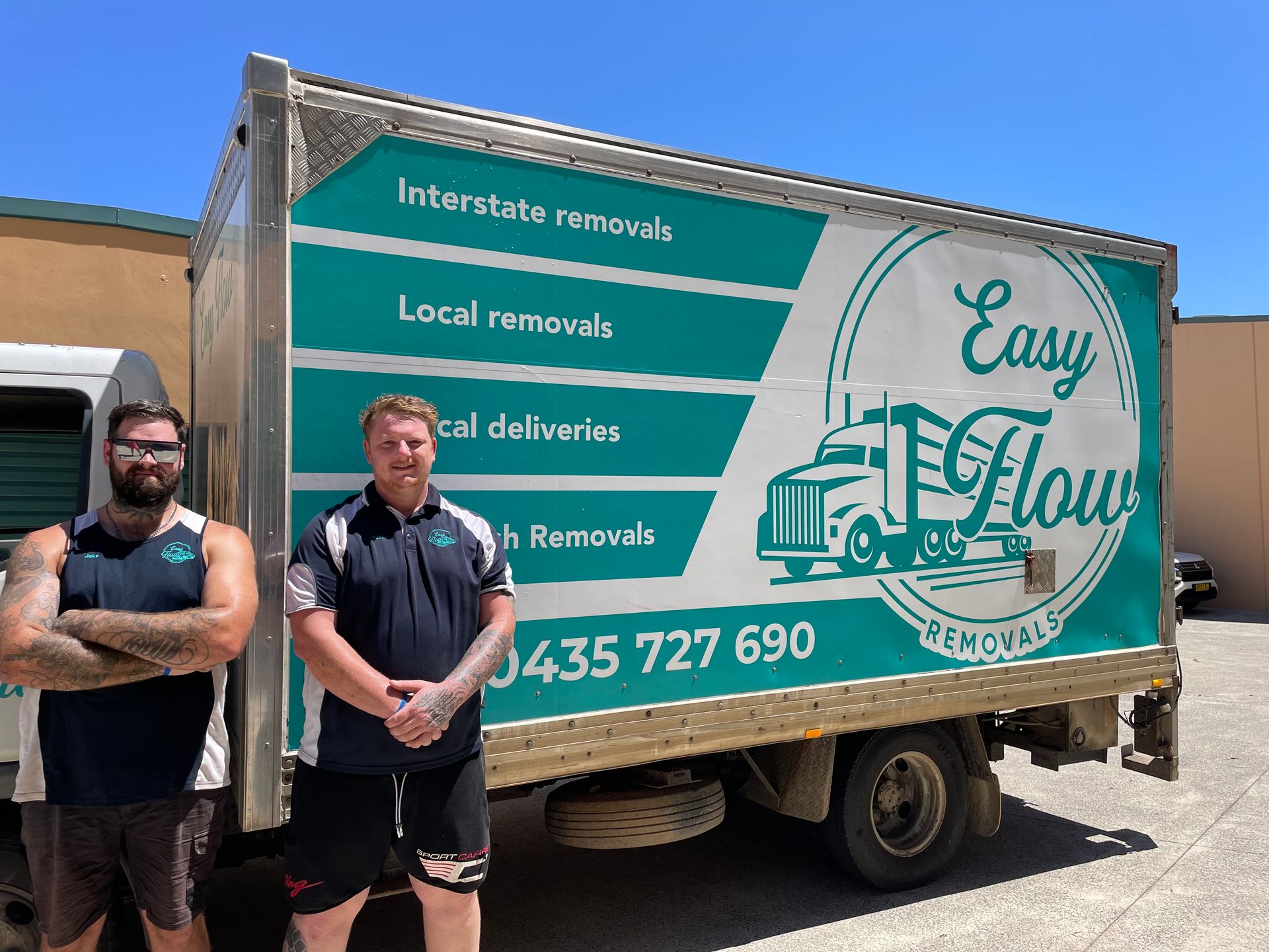 Two removalist men standing next to a green and white moving truck in Port Macquarie