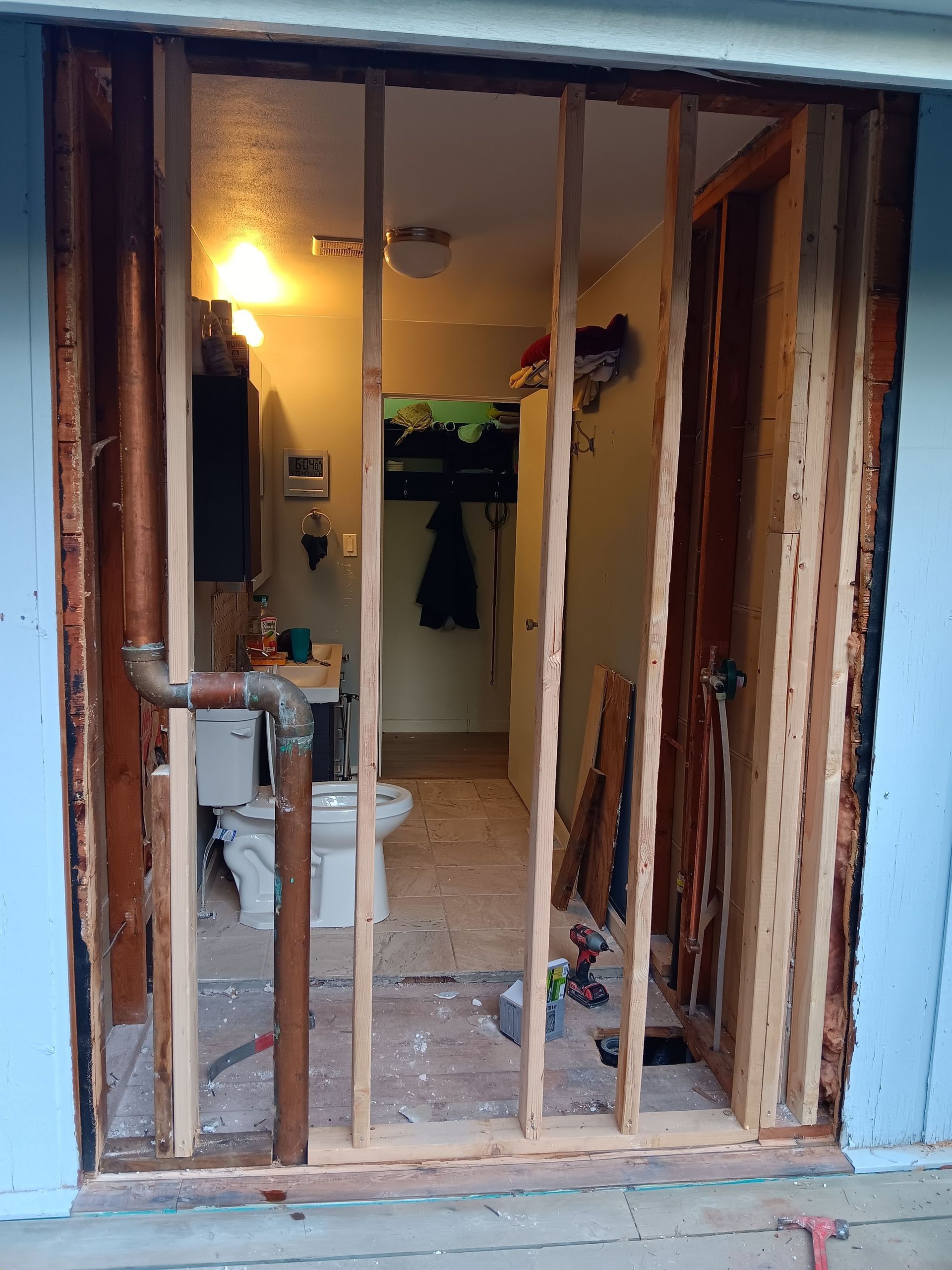 Open doorway with exposed wall studs, leading to a bathroom with a toilet and sink.