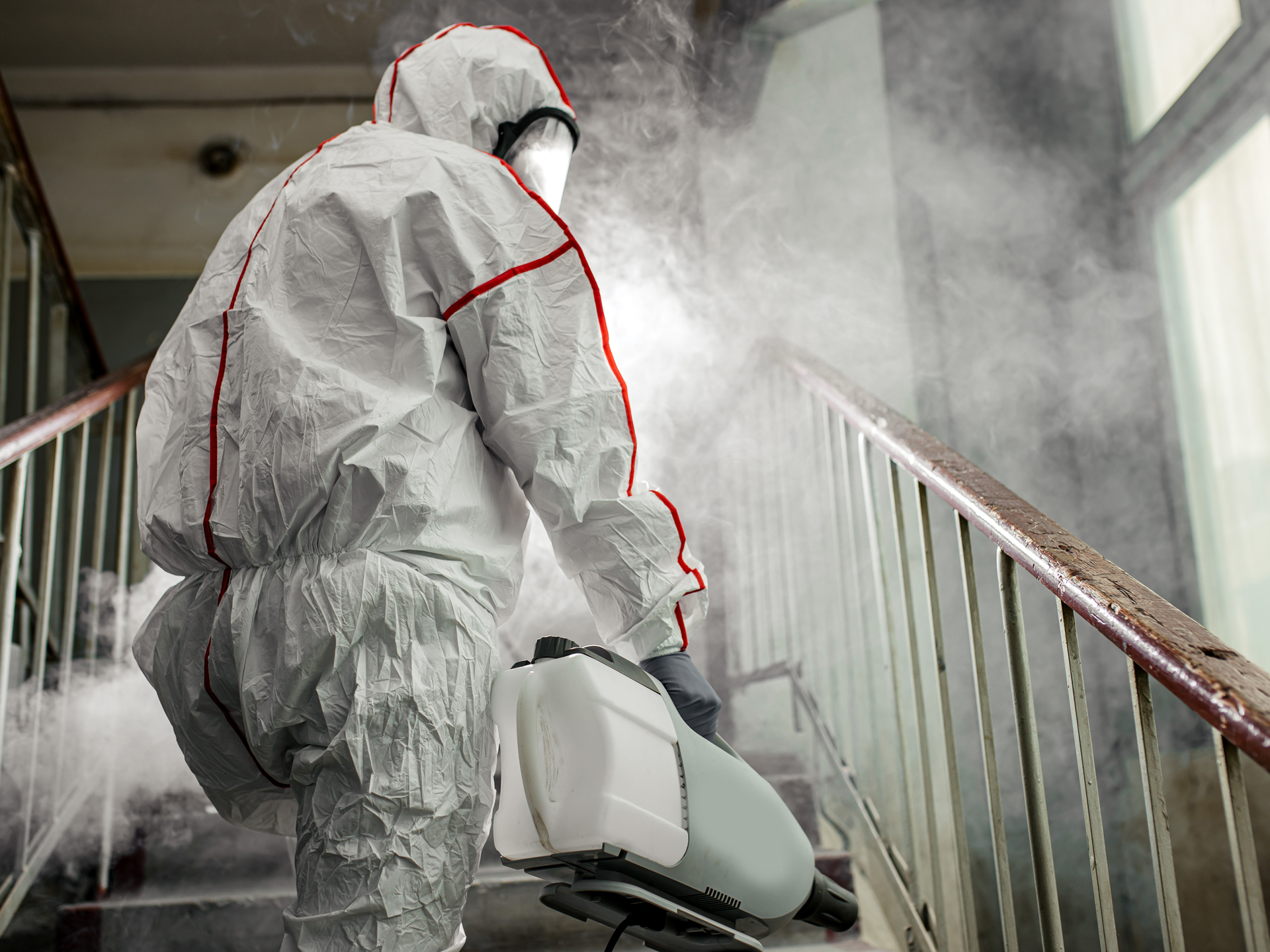 Technician in protective gear cleaning a stairway, representing biohazard cleanup.