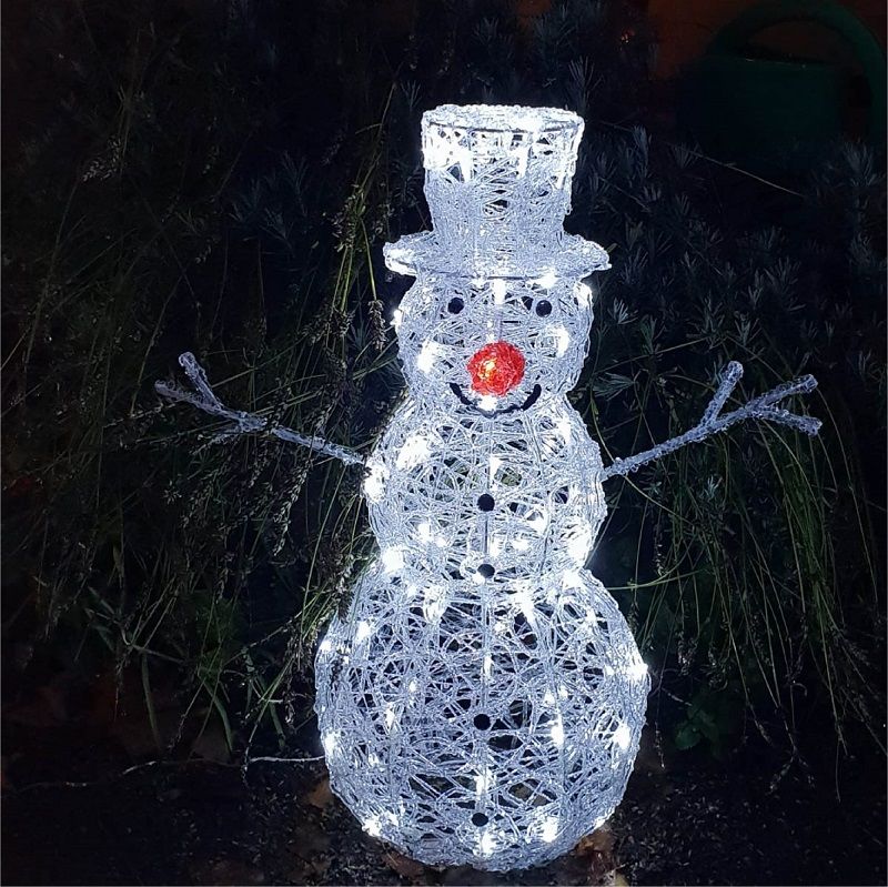 Ein Schneemann mit Zylinder und roter Nase sitzt im Gras.