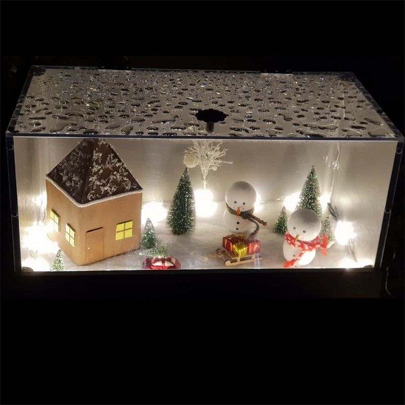 Eine Weihnachtsszene mit einem Haus, Schneemännern, Bäumen und Lichtern in einer Schachtel.