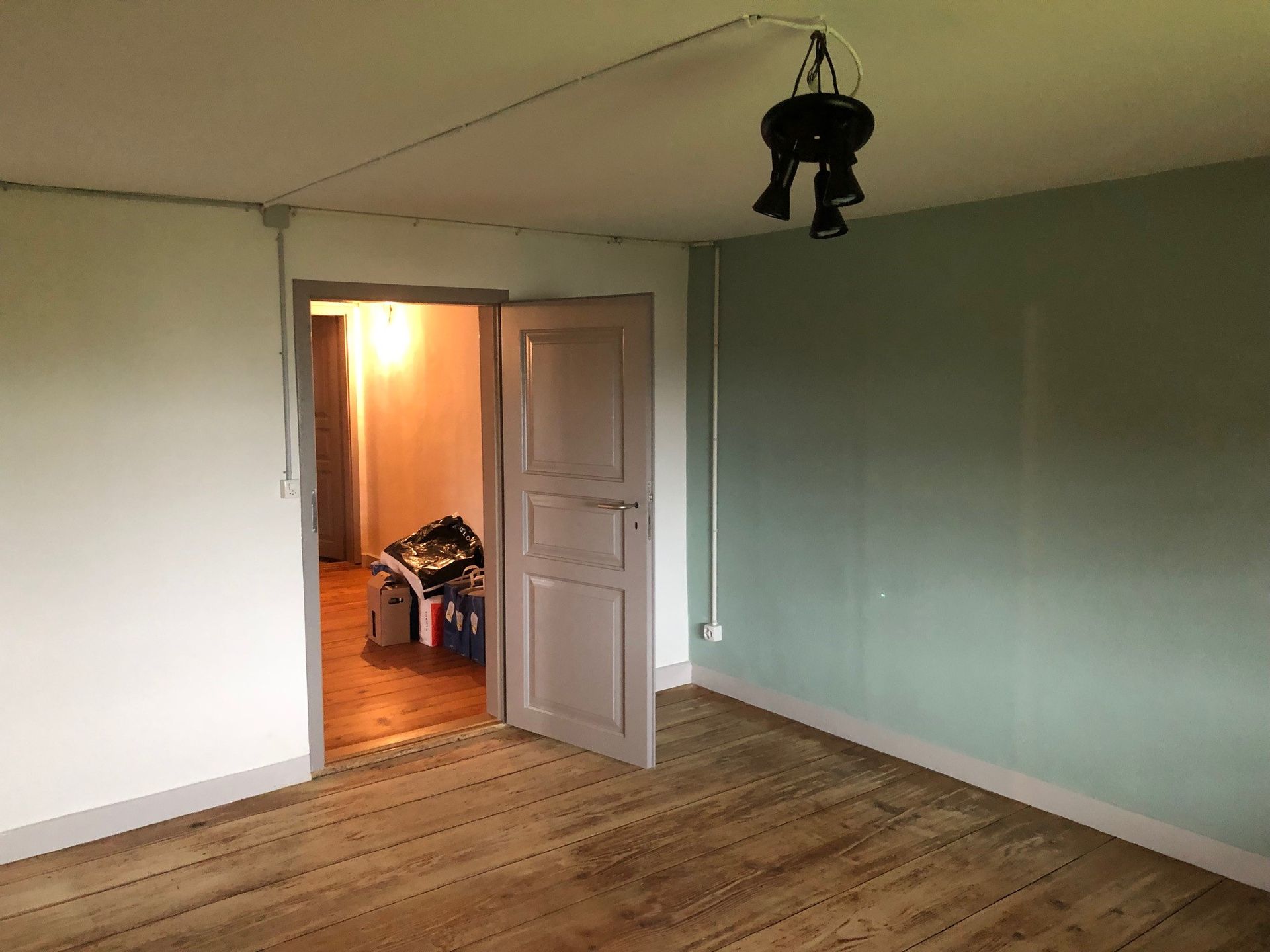 Ein leerer Raum mit Holzboden und einer Tür, die zu einem Zimmer führt.