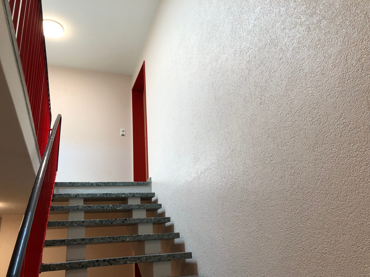 Eine Treppe mit einem roten Geländer und einer weissen Wand